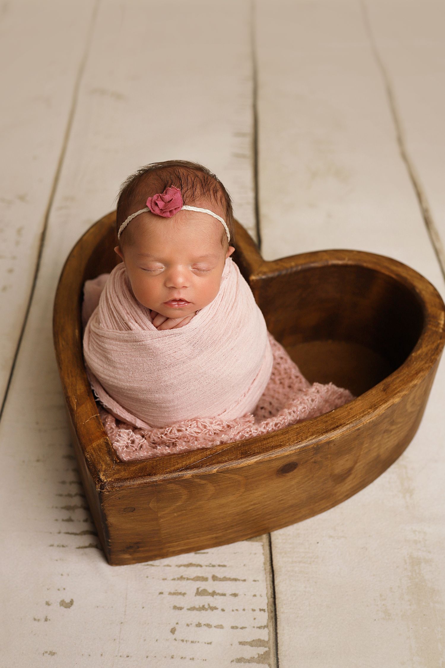 Unique newborn portrait showing a heart-shaped wooden bowl as a prop against a rustic white backdrop.