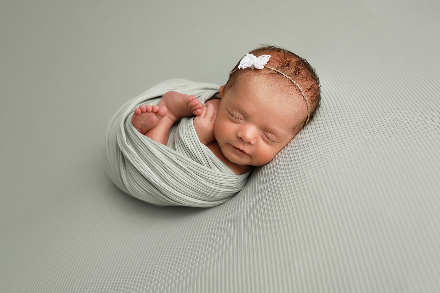 newborn photography in Utah county. A peaceful newborn baby swaddled in a soft gray wrap against a neutral backdrop.