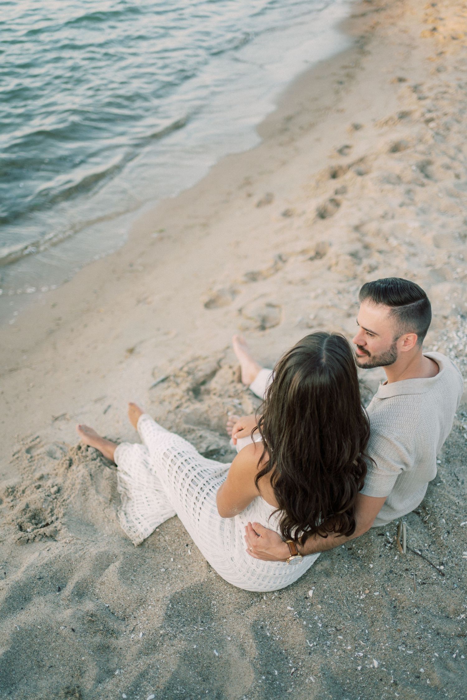 Couple relaxes together on a sandy beach beside turquoise waters during a romantic seaside moment.