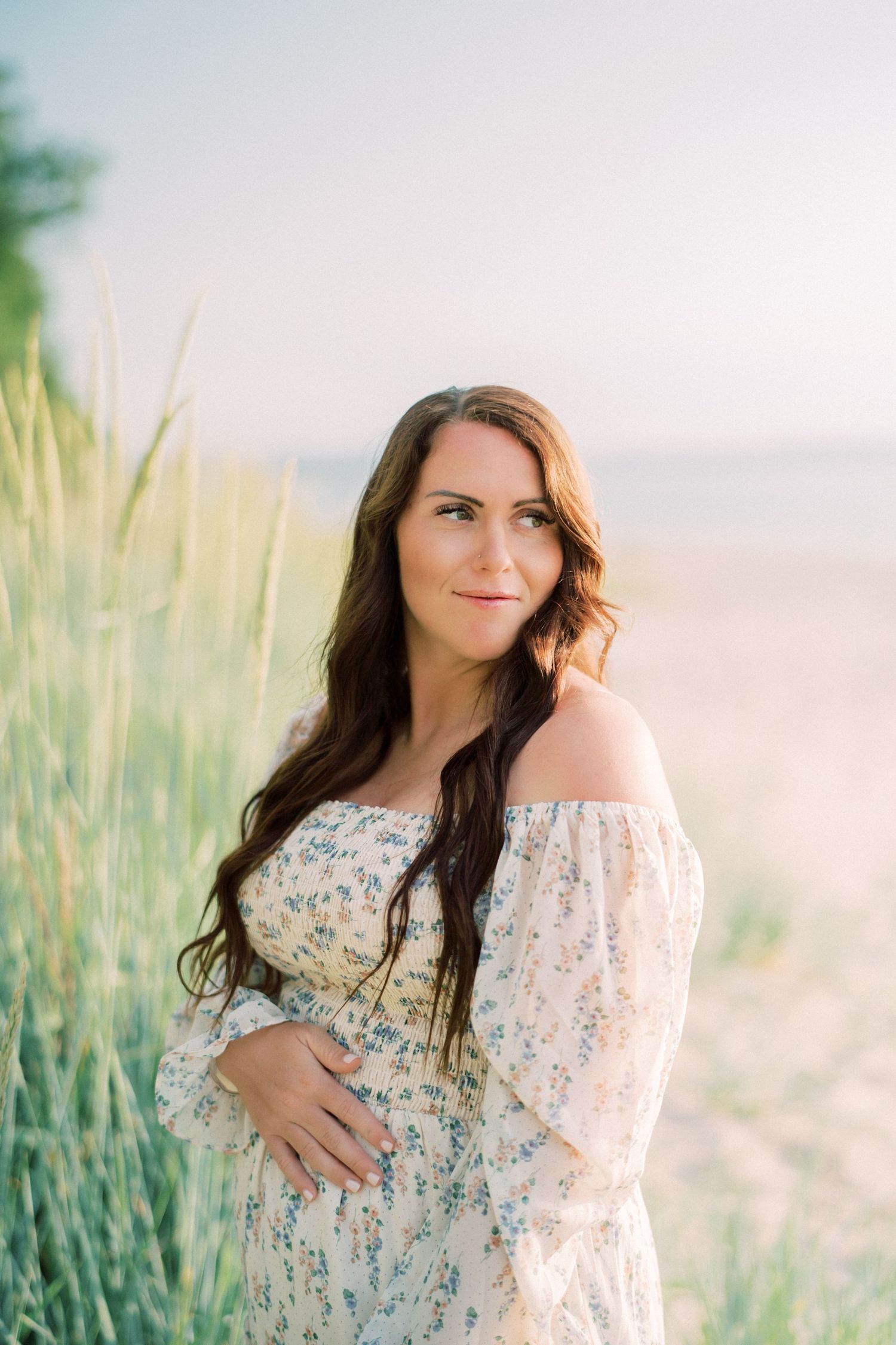 Woman in white shirt and ripped jeans walks along serene beach shoreline at sunset.