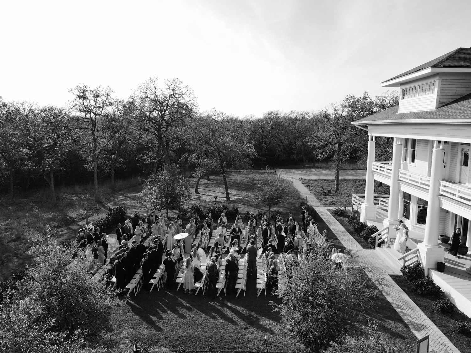 Vintage black and white photograph showing a large group of people gathered outside a stately colonial style building.