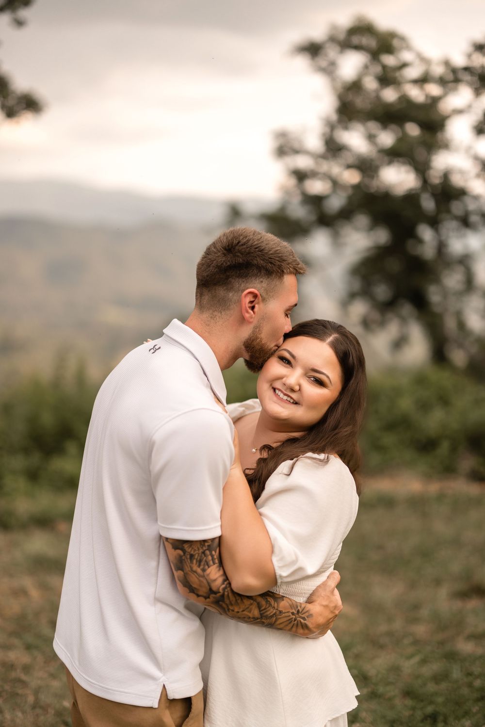 Romantic couple embraces in an outdoor setting during golden hour with natural landscape in the background.