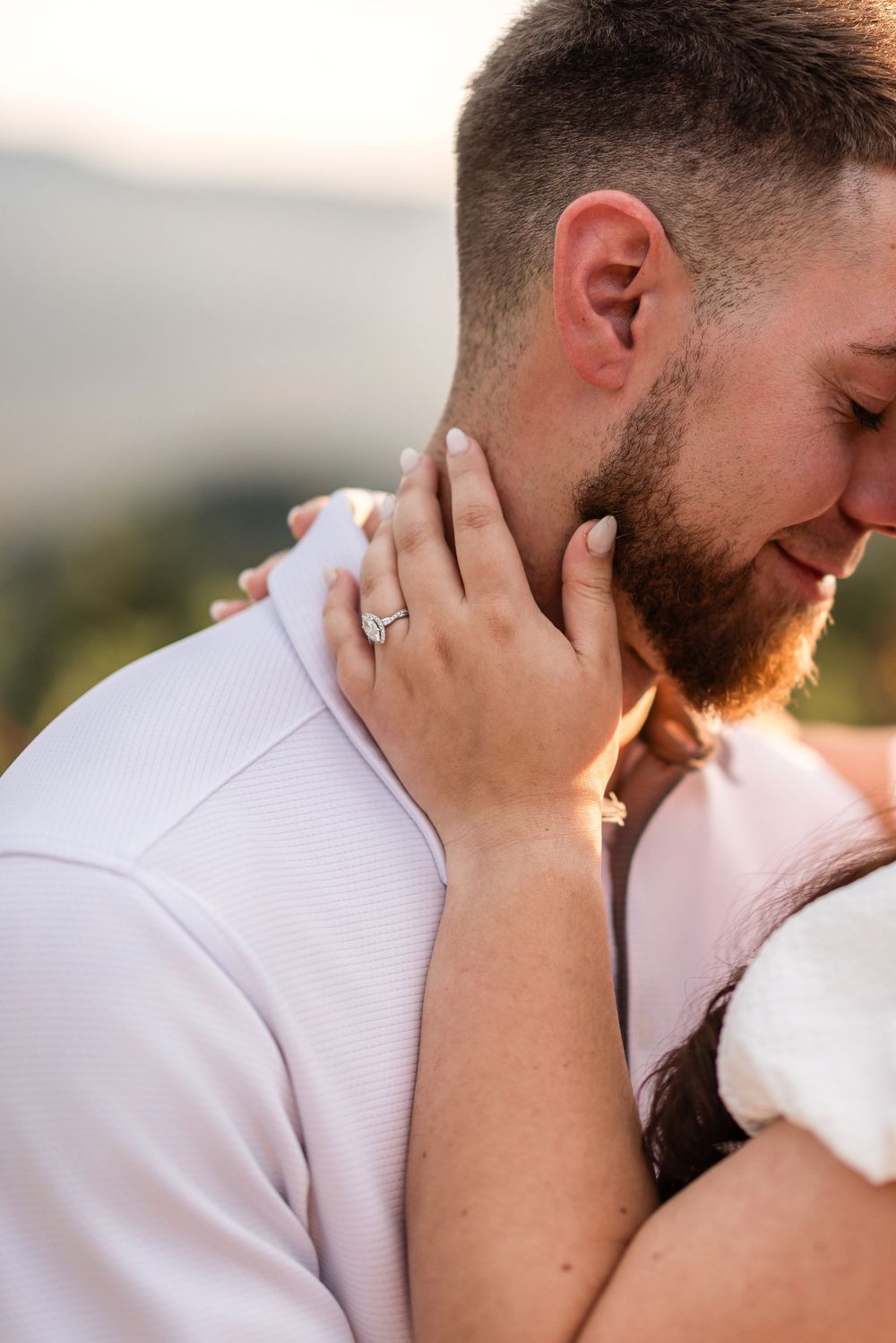 Close-up of newly engaged couple embracing outdoors, showing diamond ring and groom's ginger beard.