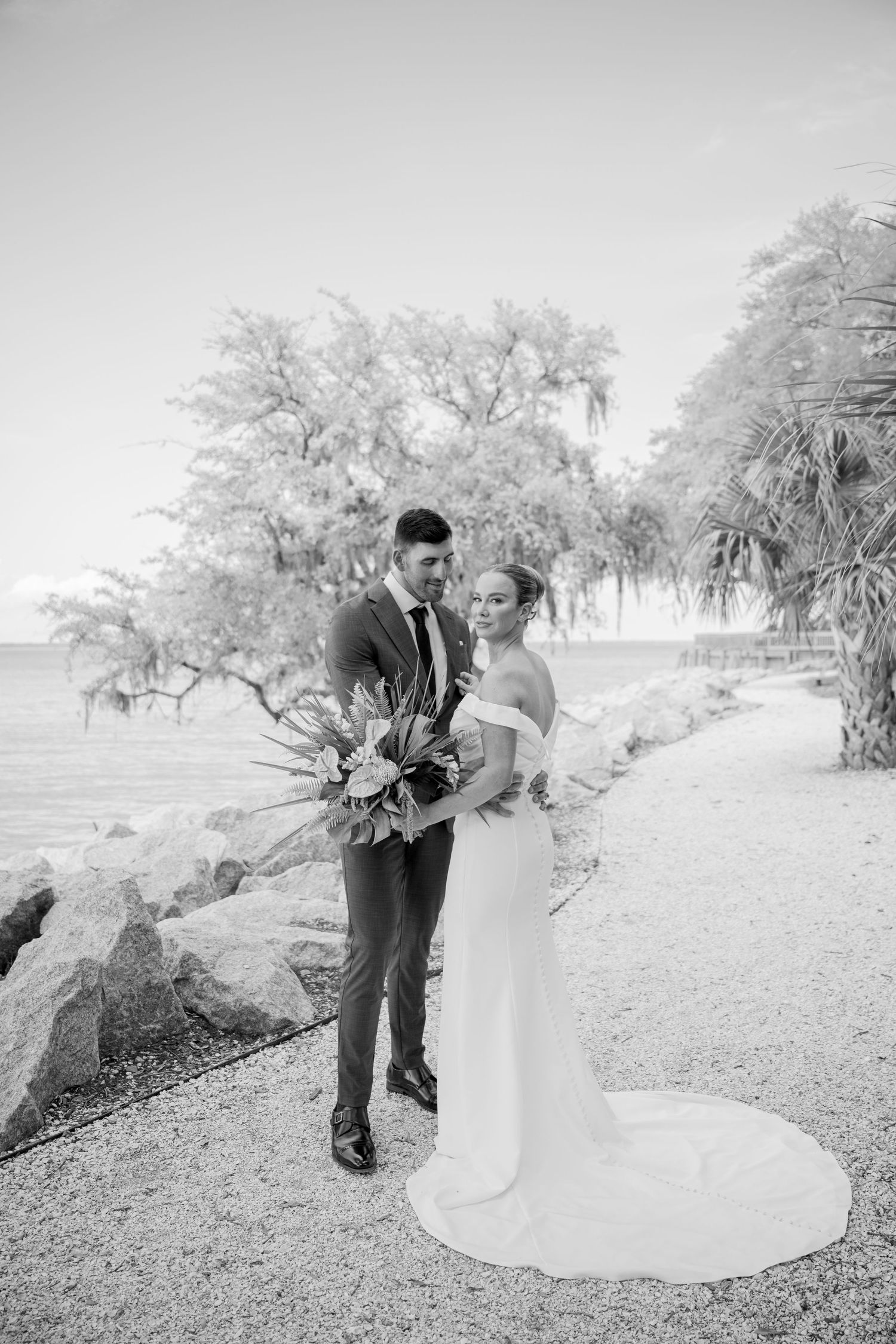 A romantic black and white wedding photo series shows a couple in formalwear embracing outdoors under snow-covered trees.