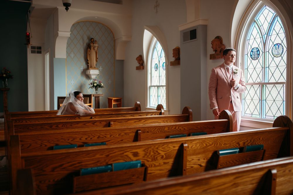 Sunlight streams through stained glass windows in a small church with wooden pews and arched architecture.