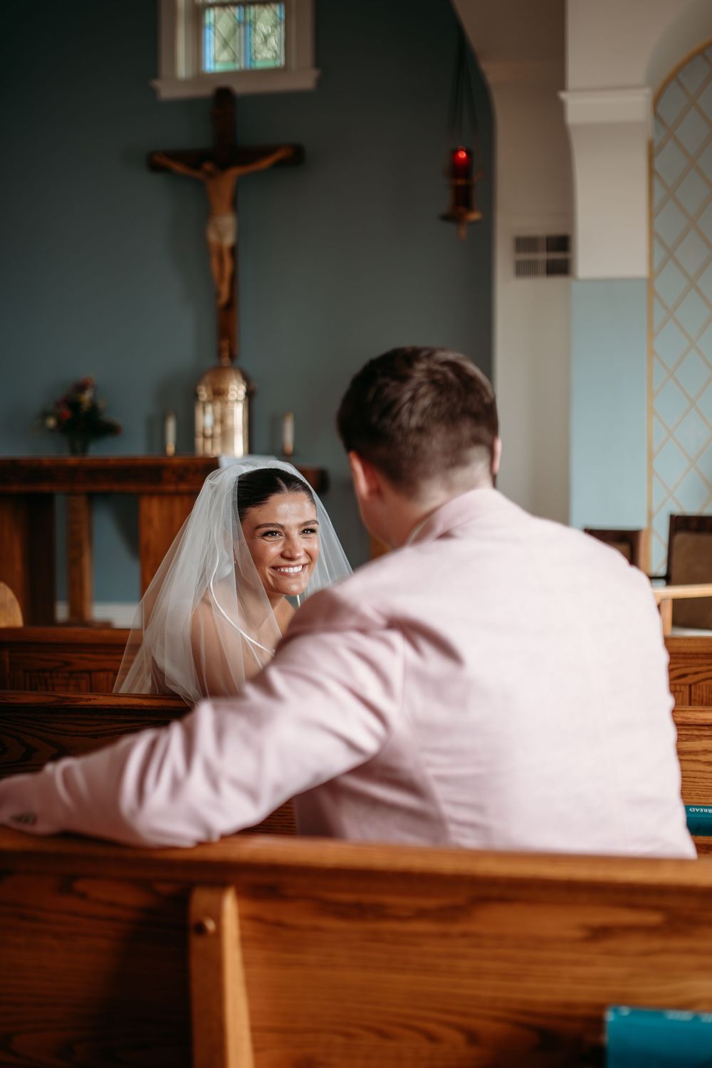 A couple shares a tender moment sitting together in a church pew while a crucifix hangs in the background.