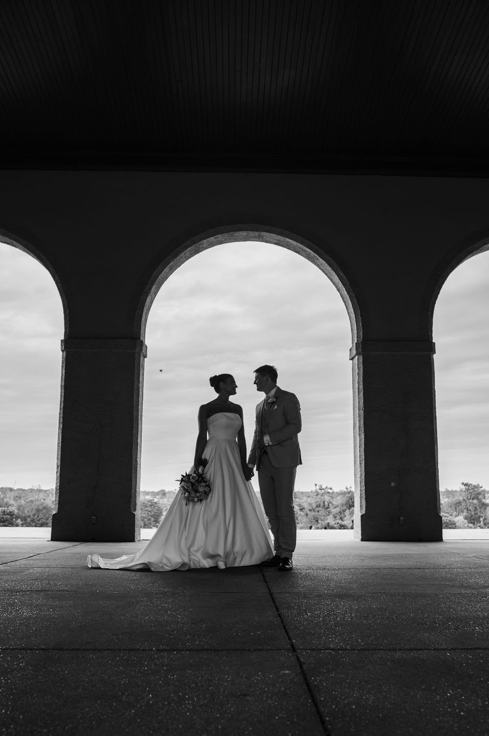 Black and white silhouettes of a couple sitting under stone arches create an artistic architectural wedding scene.