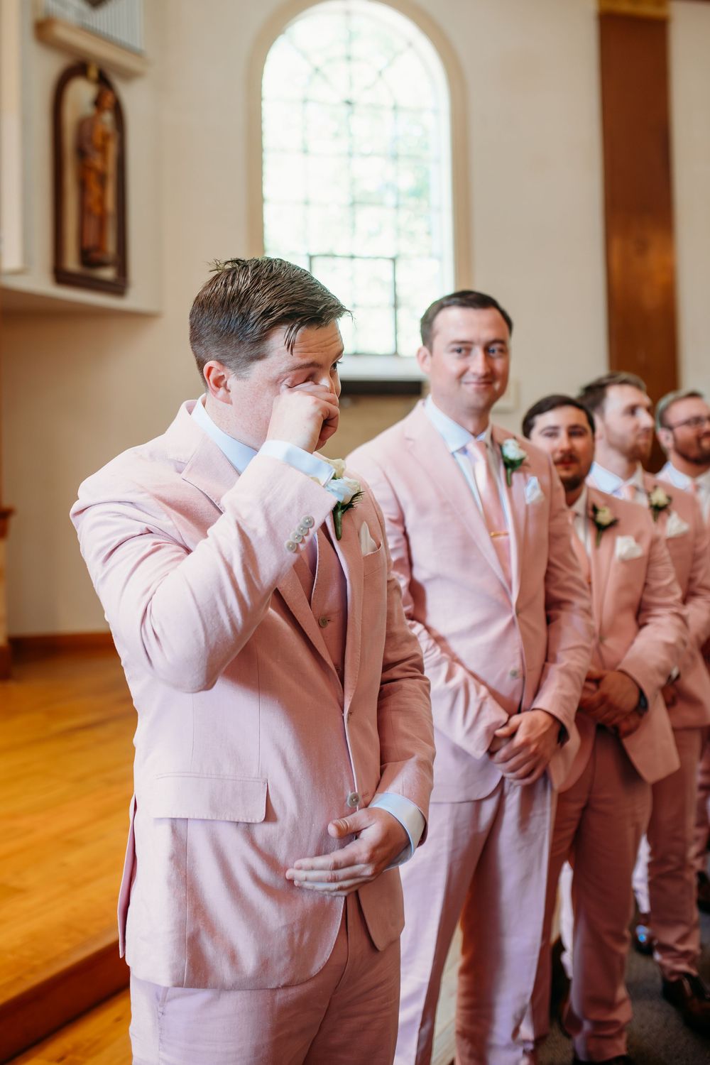 Row of groomsmen in light pink suits dabbing in a coordinated sequence at a wedding venue.