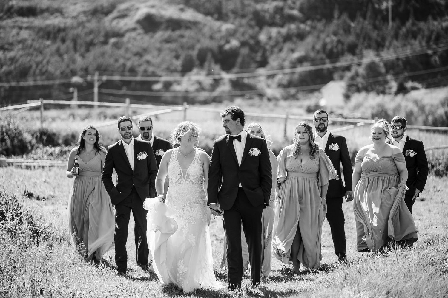 Black and white wedding party walking together through a grassy field on a sunny afternoon.