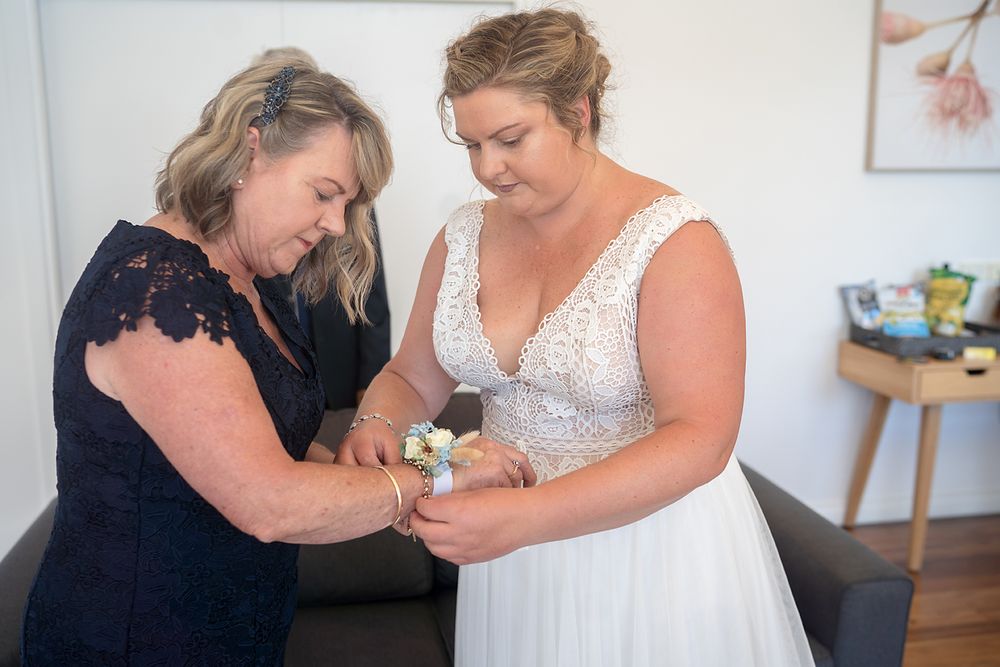 Two women in contrasting navy and white dresses help with wedding day preparations in a bright interior setting.
