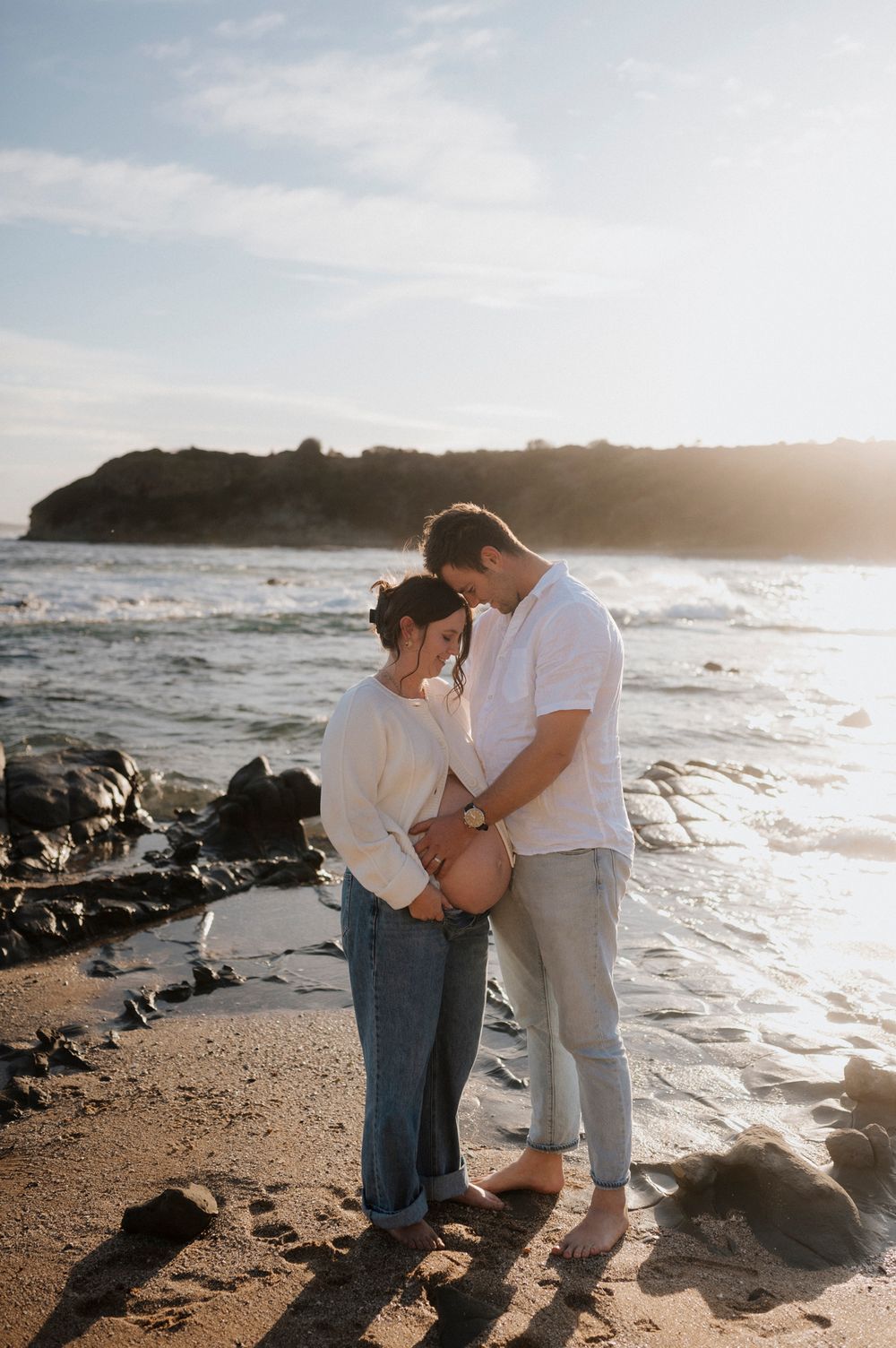 Two people share an intimate moment while standing together on a beach during golden hour.