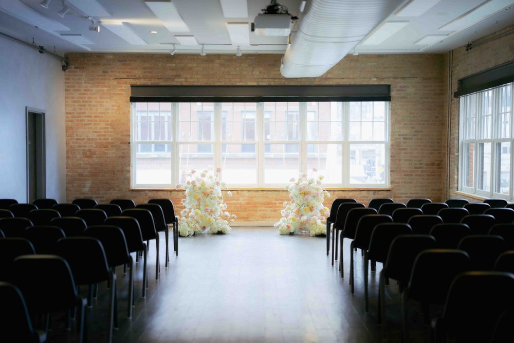 Wedding ceremony space with rows of black chairs and natural light streaming through large windows.