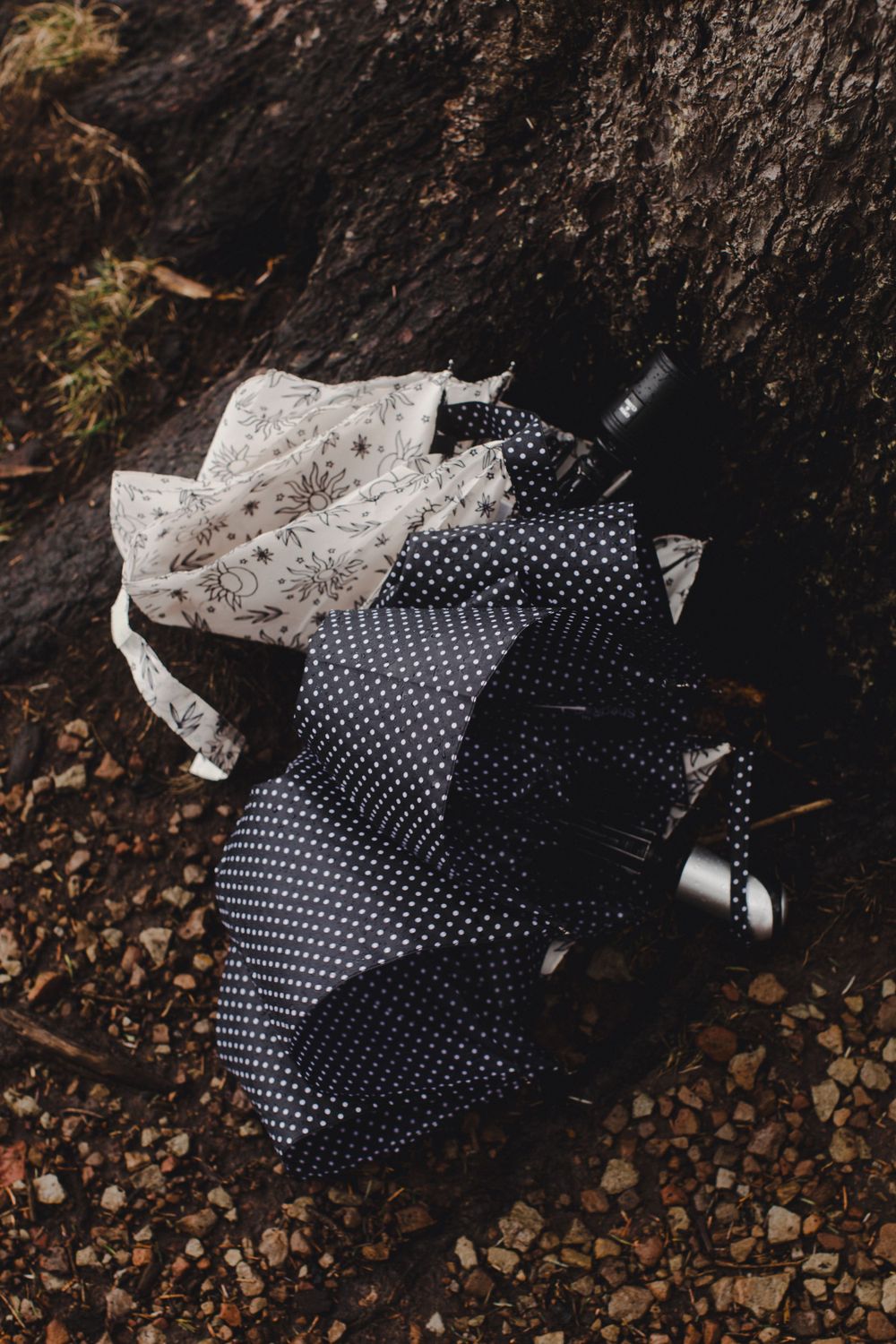 A polka dot dress and white floral garment lying on dark soil and rocks.