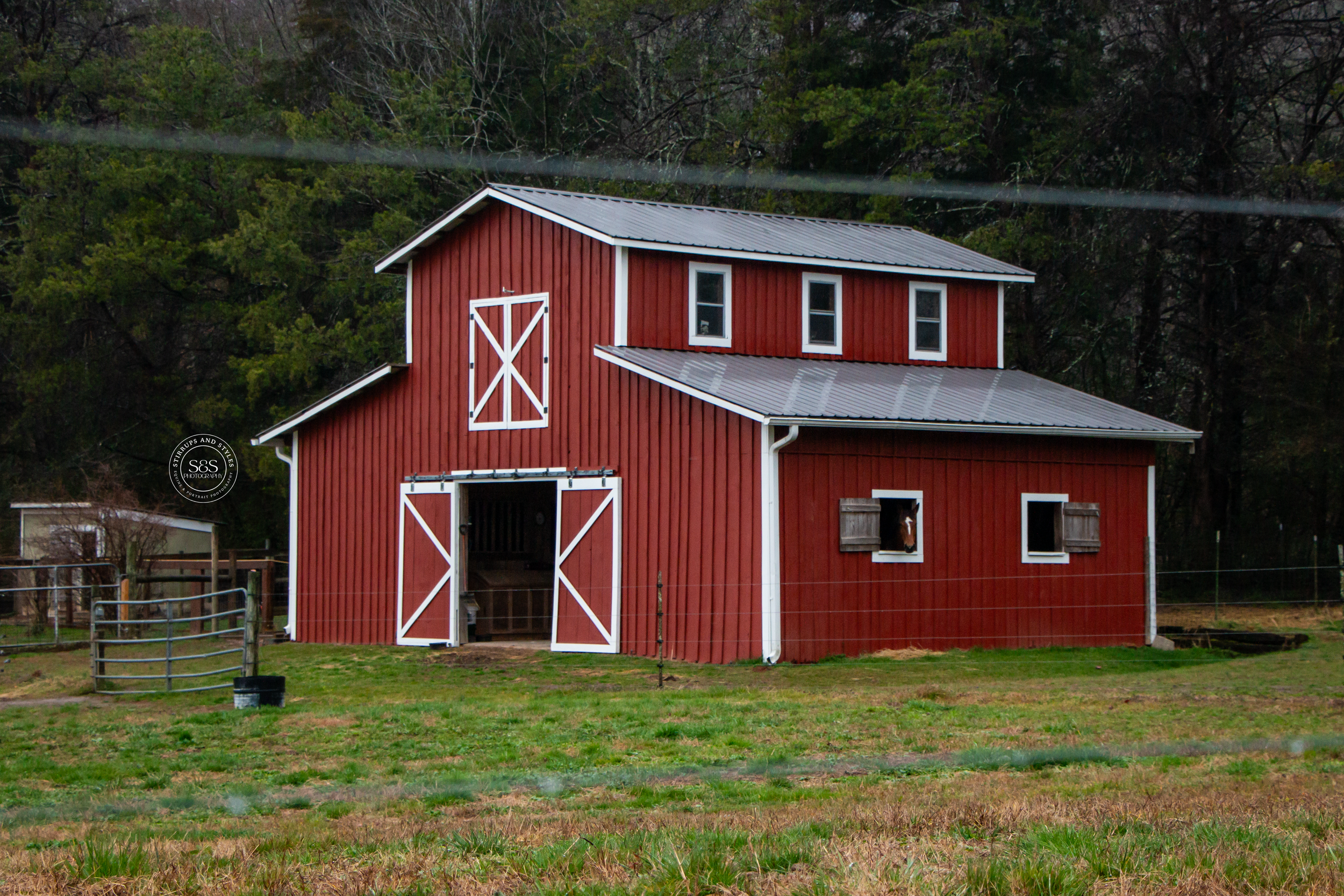 Classic red barn with white trim and double doors stands in a grassy field with rustic farmhouse architecture.