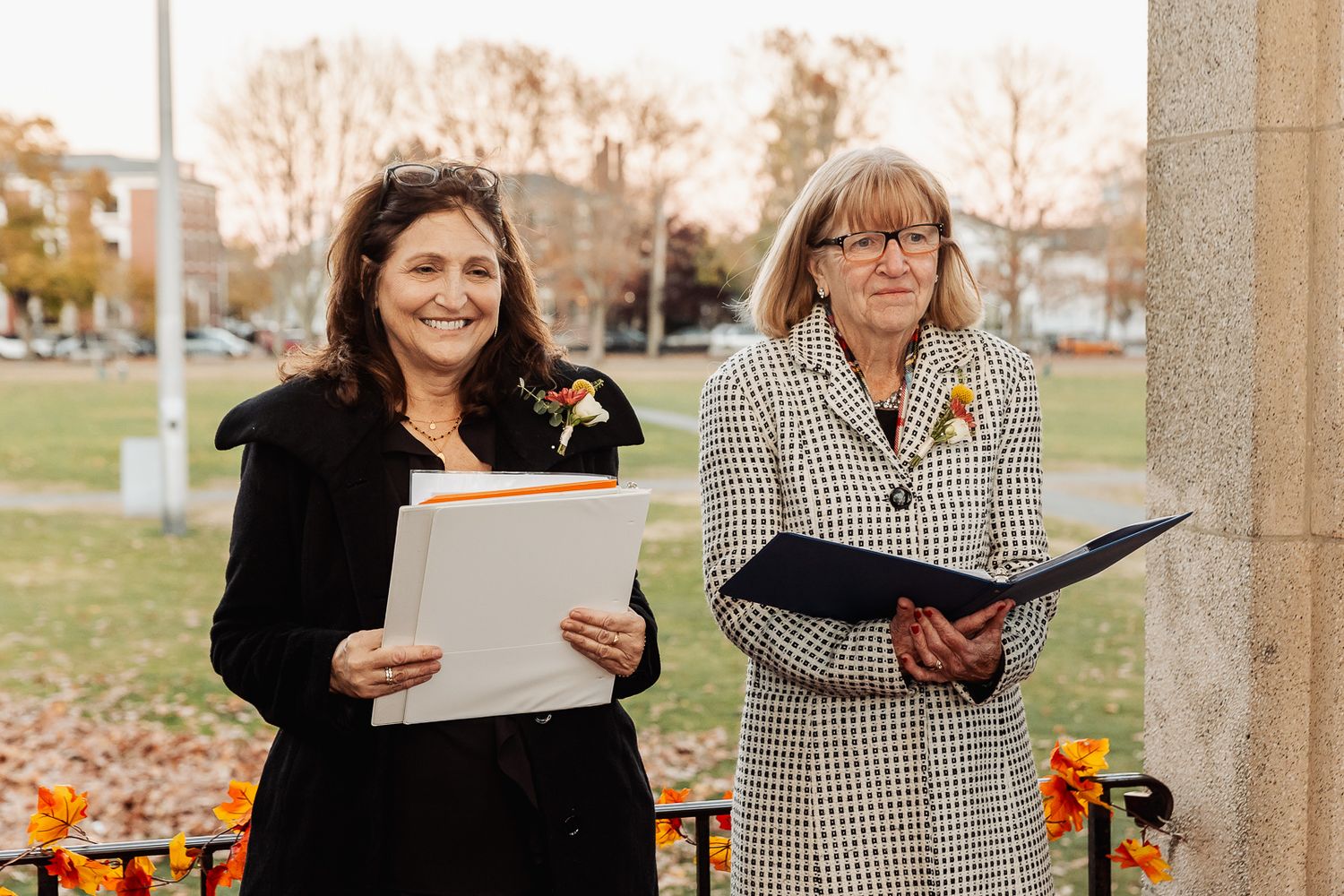 Two ceremony officials reviewing documents while standing outdoors in autumn.