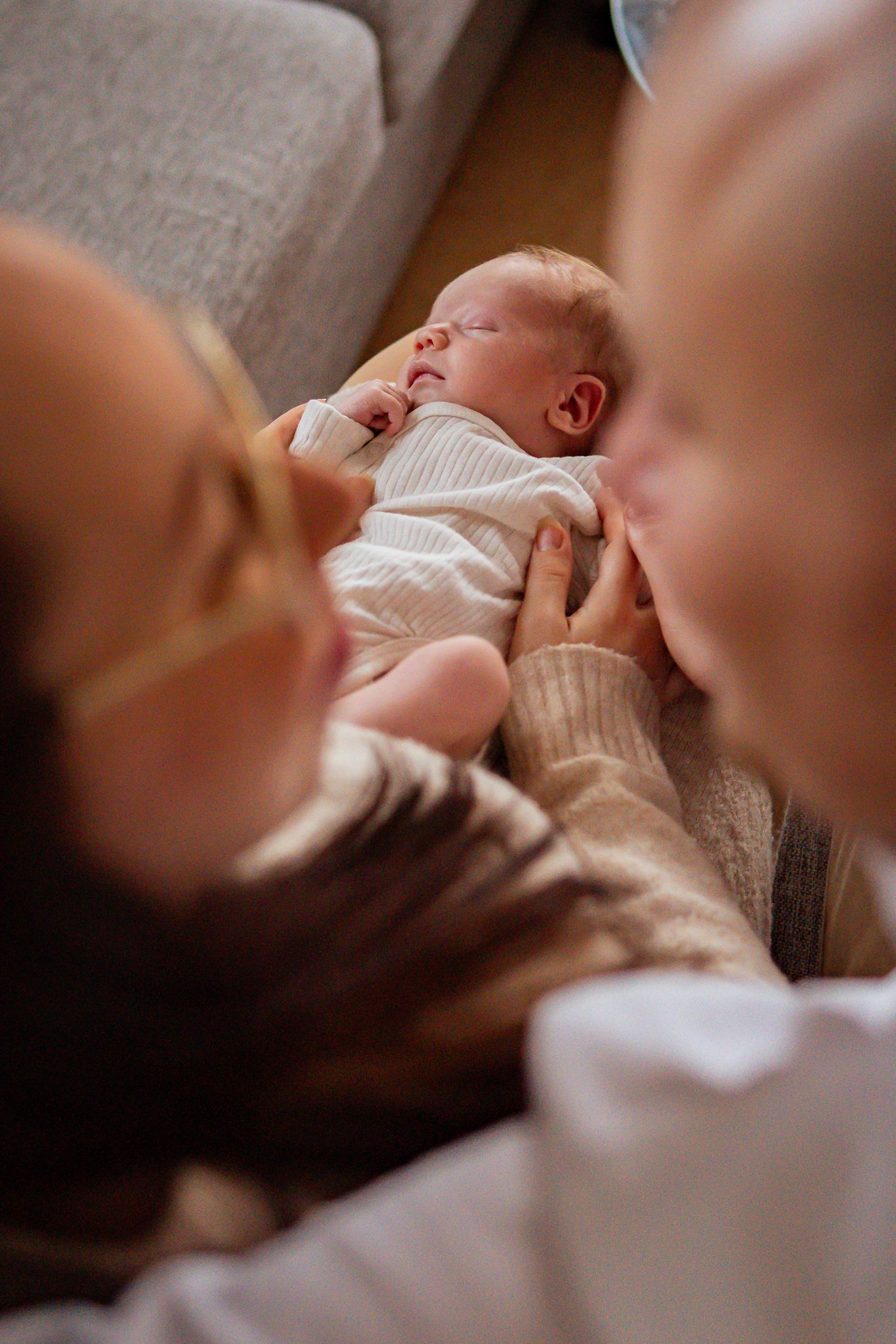 Nyfödd bebis sover fridfullt i mamma knä, föräldrarna tittar leende på varandra i förgrunden. Fotograf, nyföddfotograf, Umeå, Västerbotten