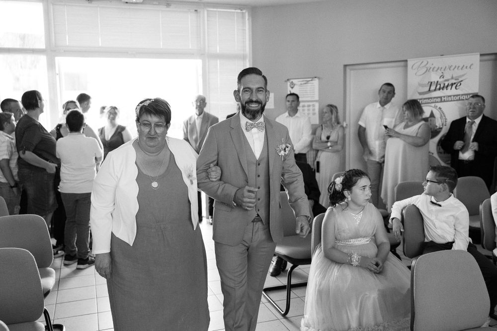 Wedding guests gather in a bright indoor reception space with rows of chairs.