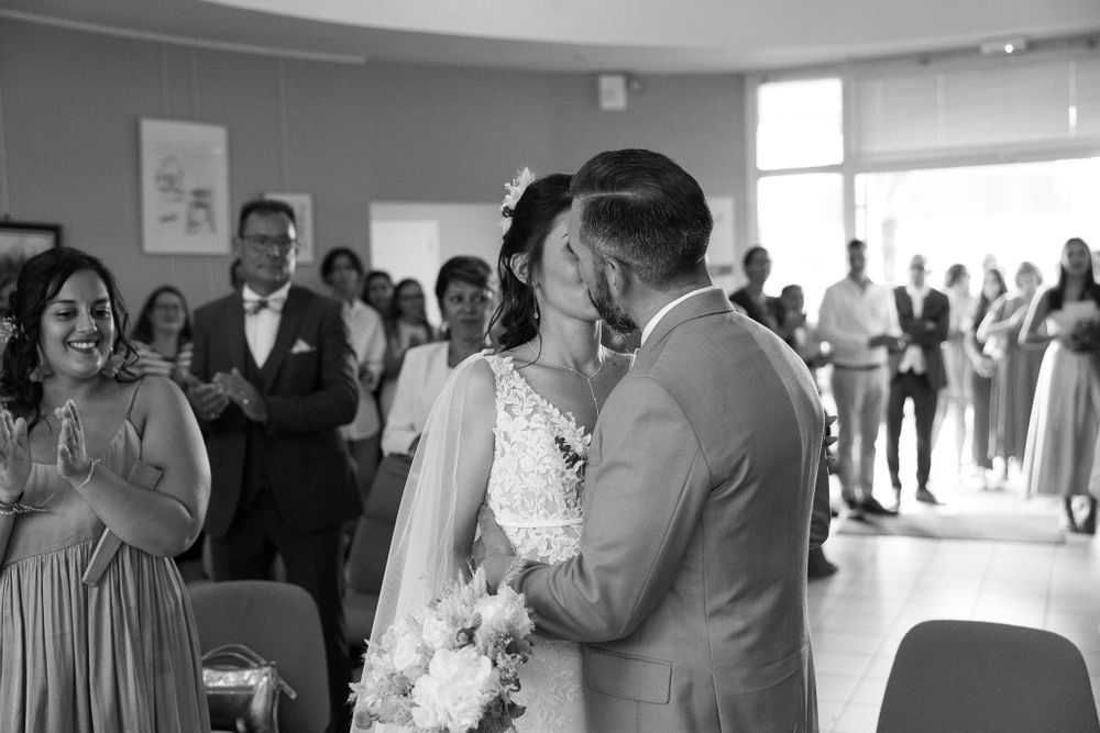 Intimate wedding ceremony moment captured in black and white with guests looking on in a bright indoor venue.