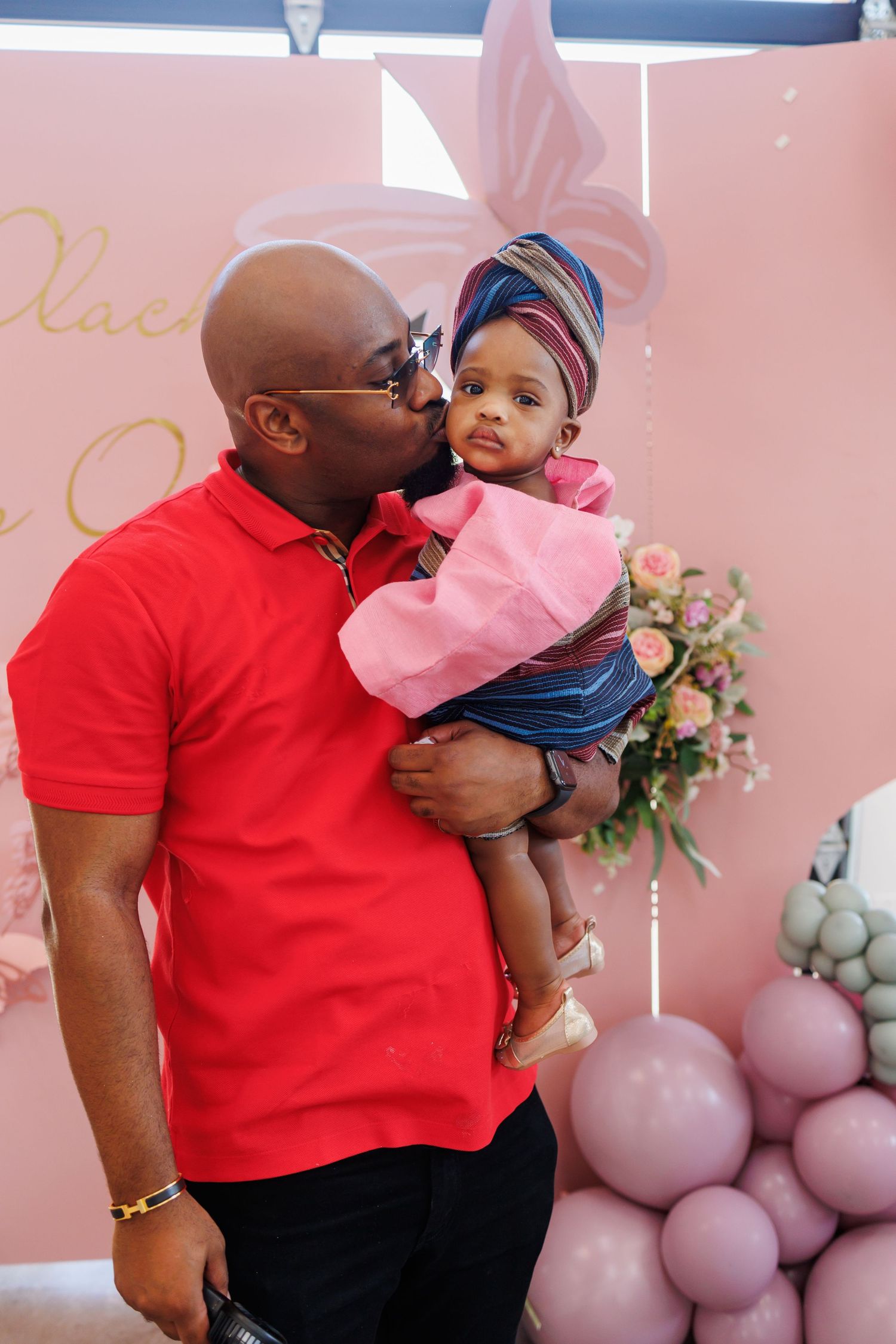 A tender moment of the birthday girl in traditional African dress captured at a pink-themed party with balloons and floral decorations