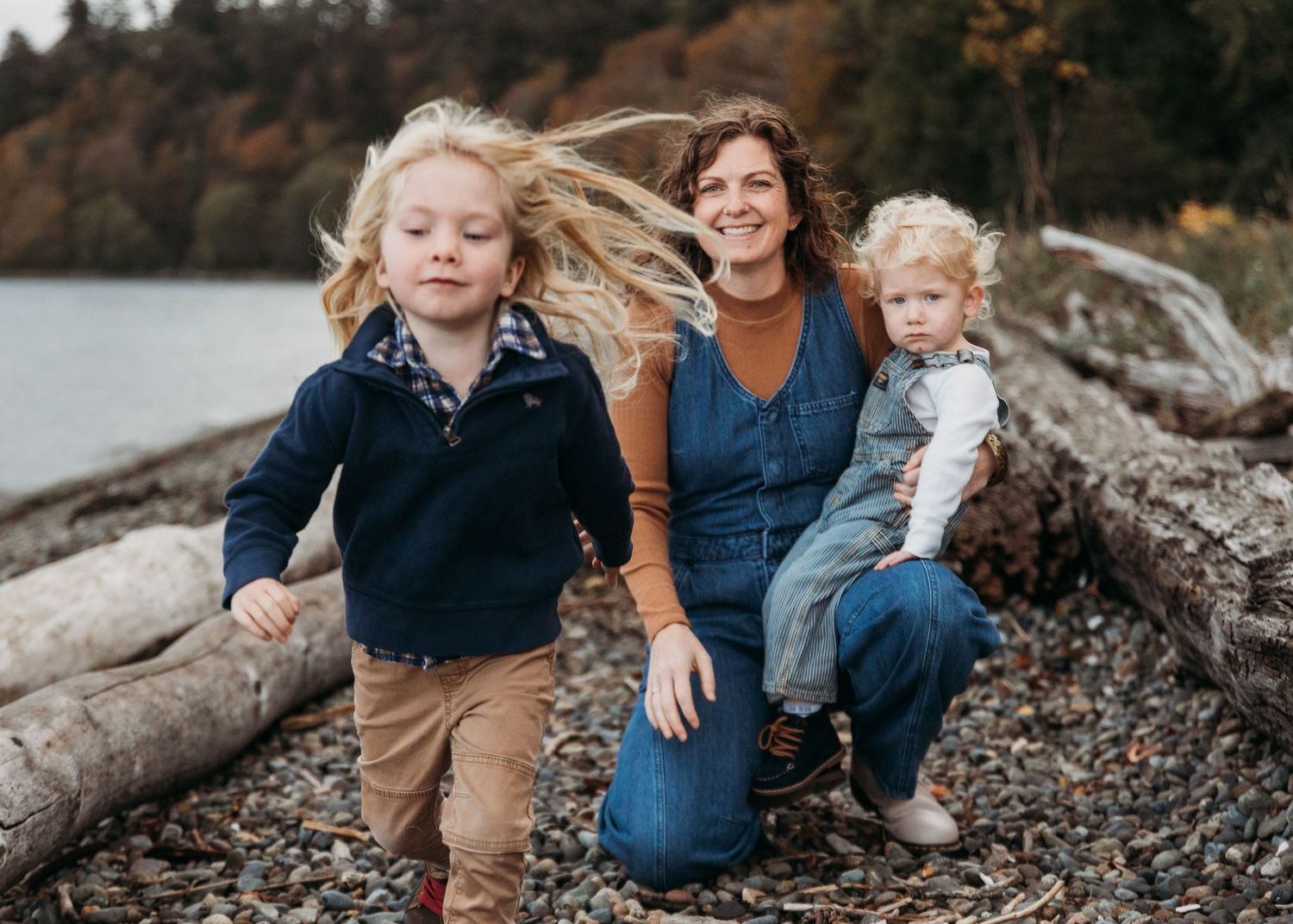 A family dressed in casual clothing sits together on driftwood at a rocky beach during sunset.