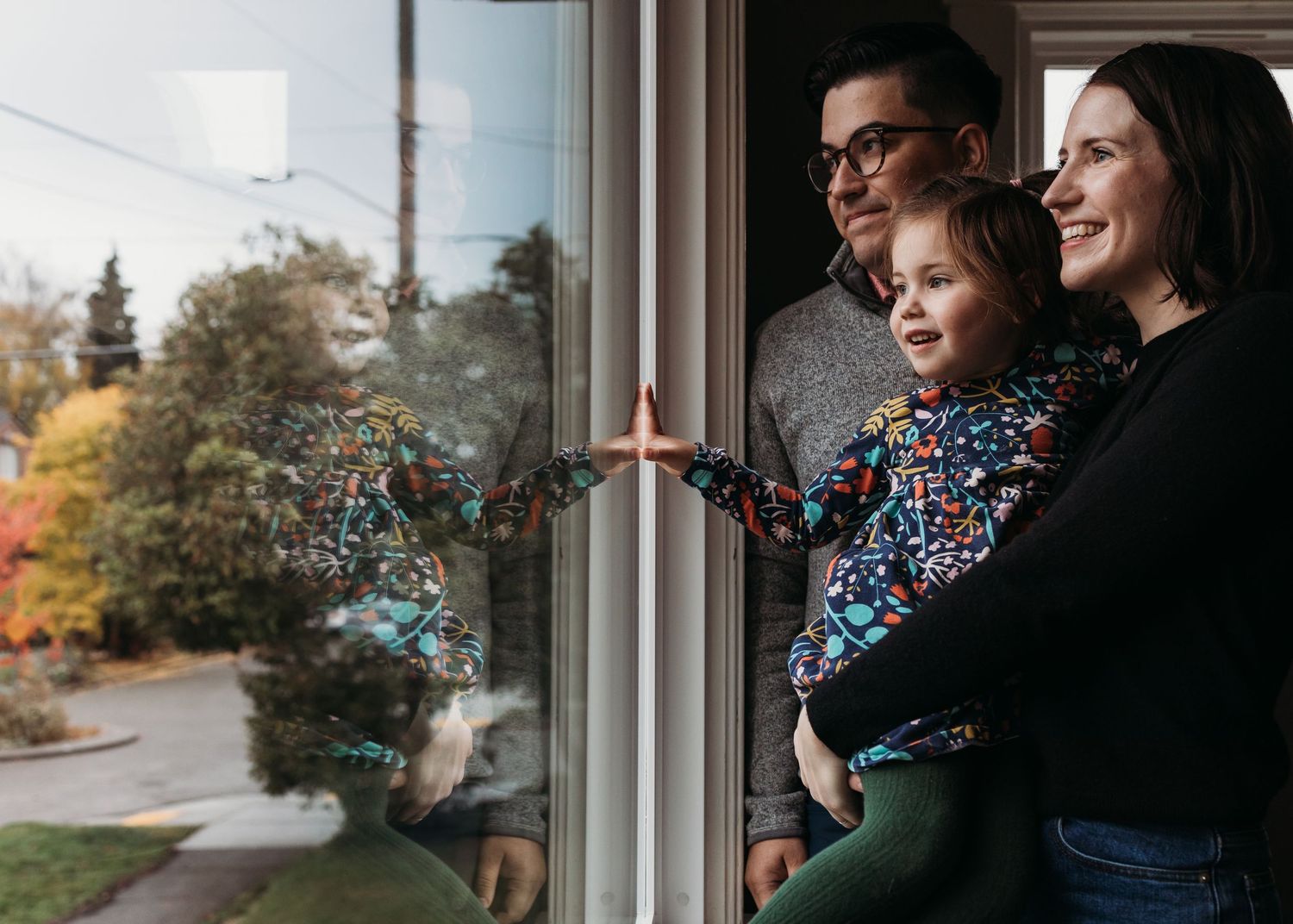 Family stands at window together blowing blue and pink confetti in celebration during autumn season.