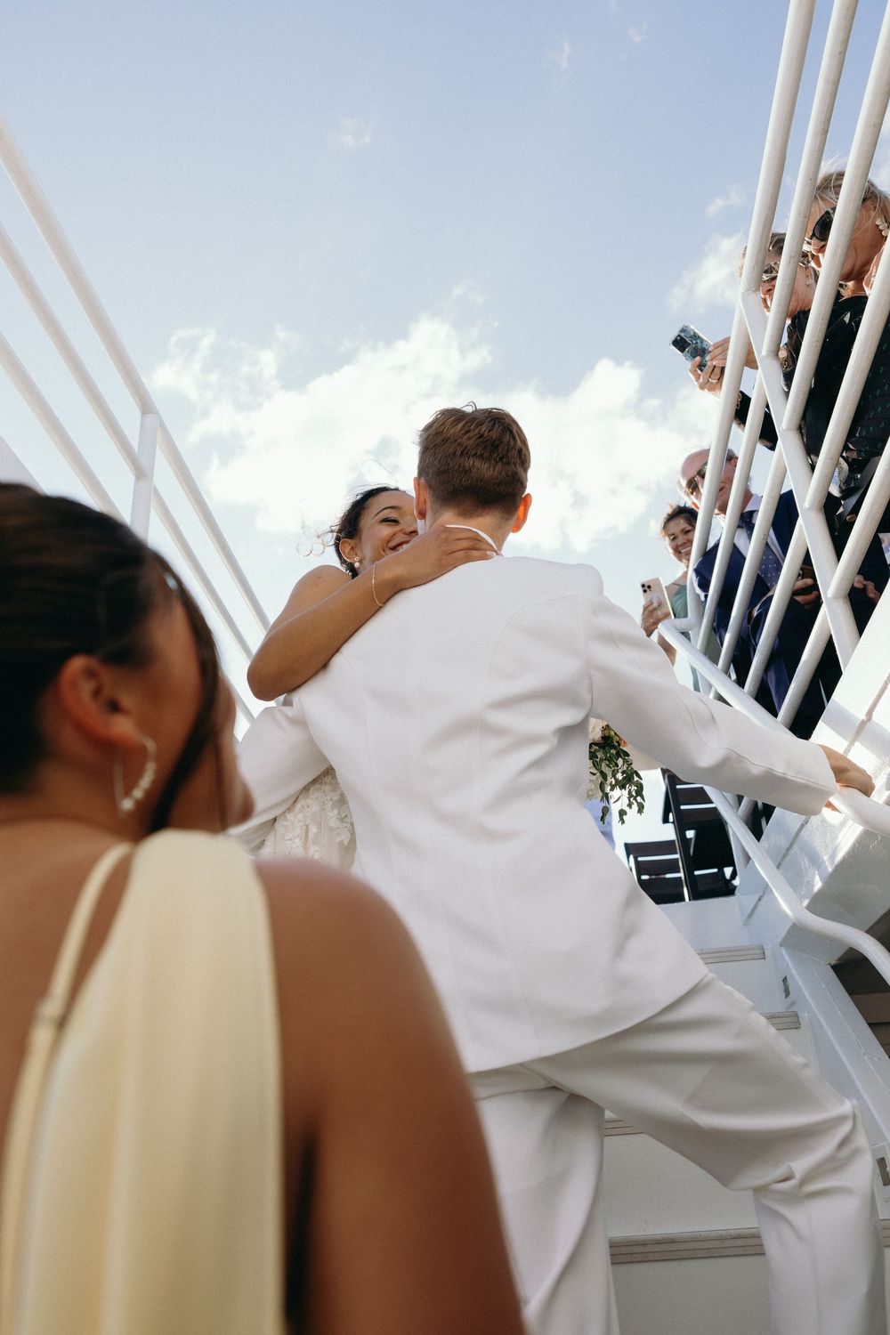 Wedding guests lean over a white ship railing to enjoy the ocean views during a nautical celebration.