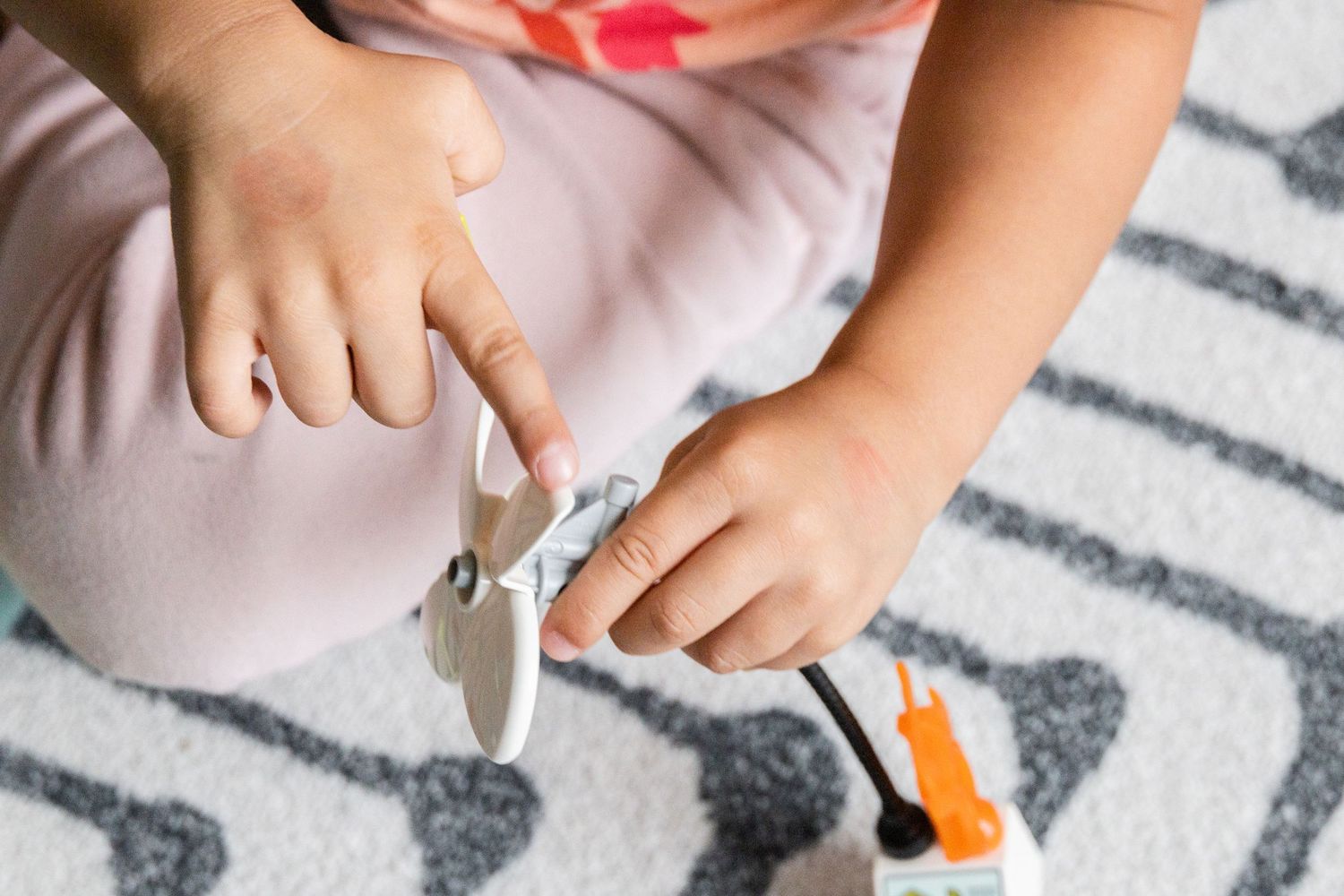 Small hands playing with scissors and craft supplies on a gray and white patterned carpet.