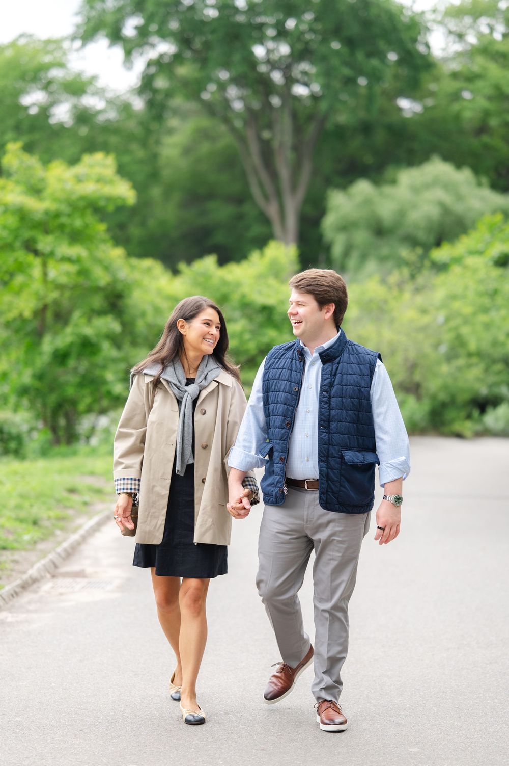 Two people walk together while holding hands along a tree-lined path on a sunny day in Central Park by best NYC proposal photographer.