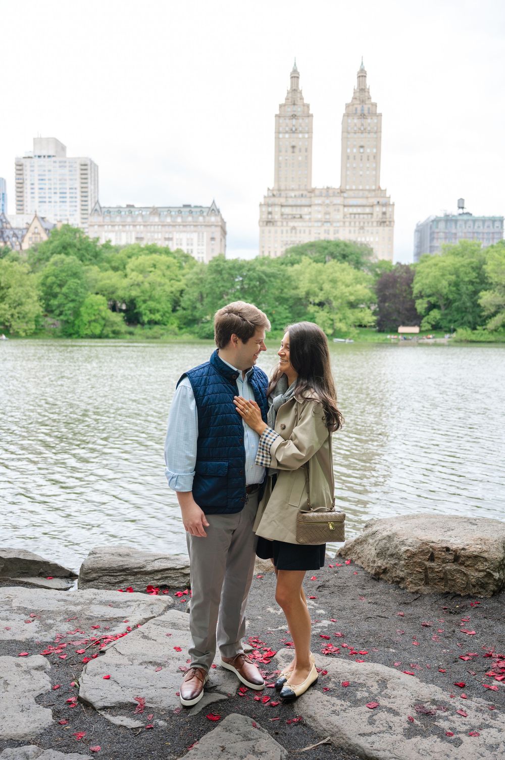 A romantic moment by the Central Park lake in New York City with the iconic San Remo towers visible in the background after a proposal