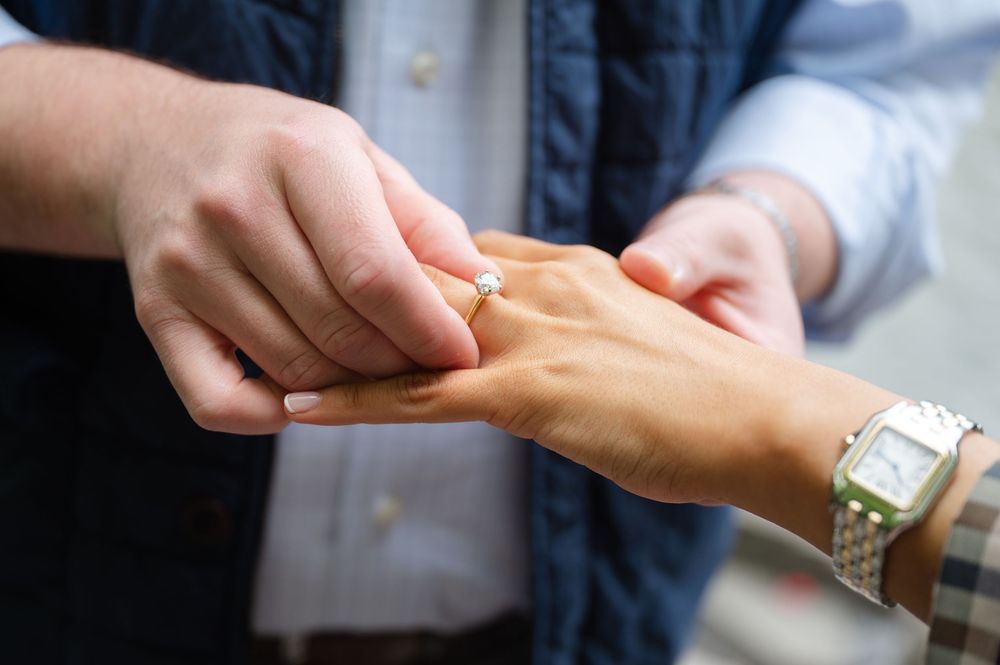 Close up of someone placing a ring on another person's hand next to a white watch.