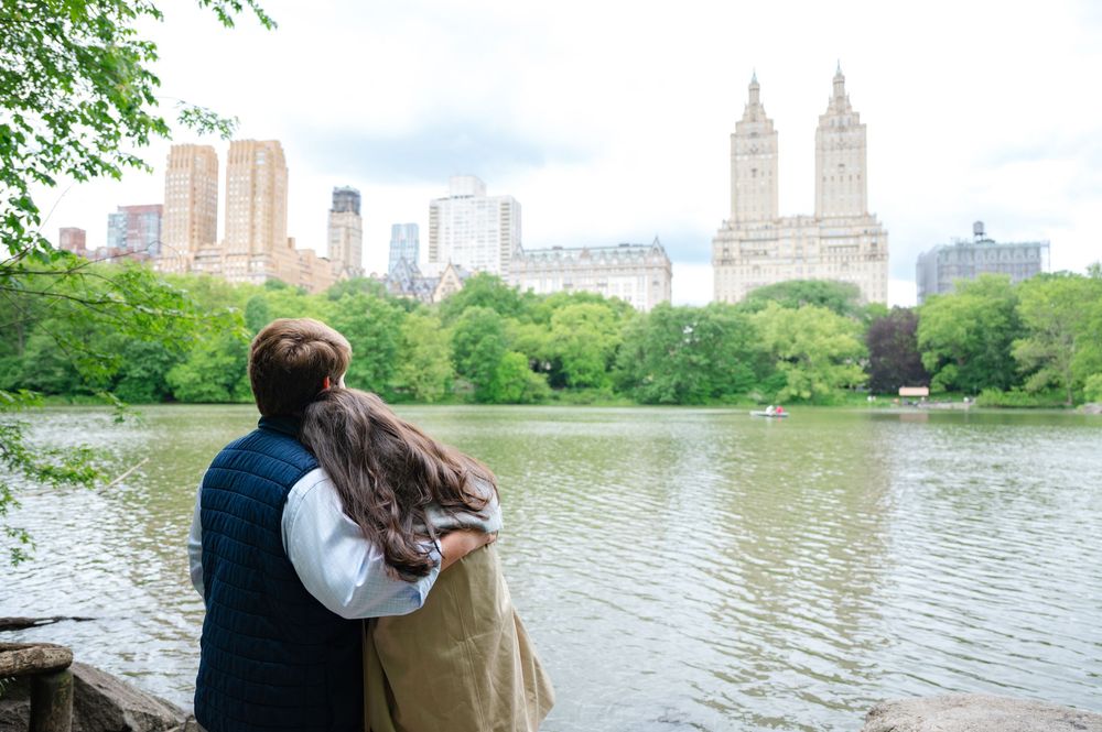 Two people embrace while enjoying a scenic view of Central Park Lake and Manhattan skyline on a spring day after their surprise NYC proposal