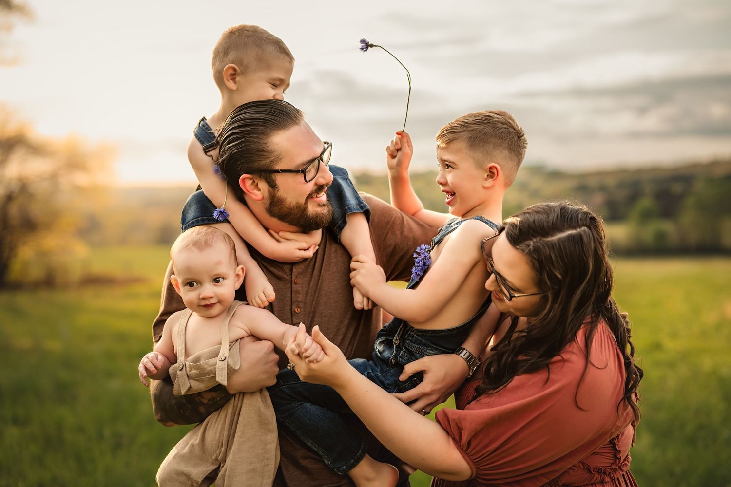 Family playing together and hugging in a grassy field during golden hour sunset.