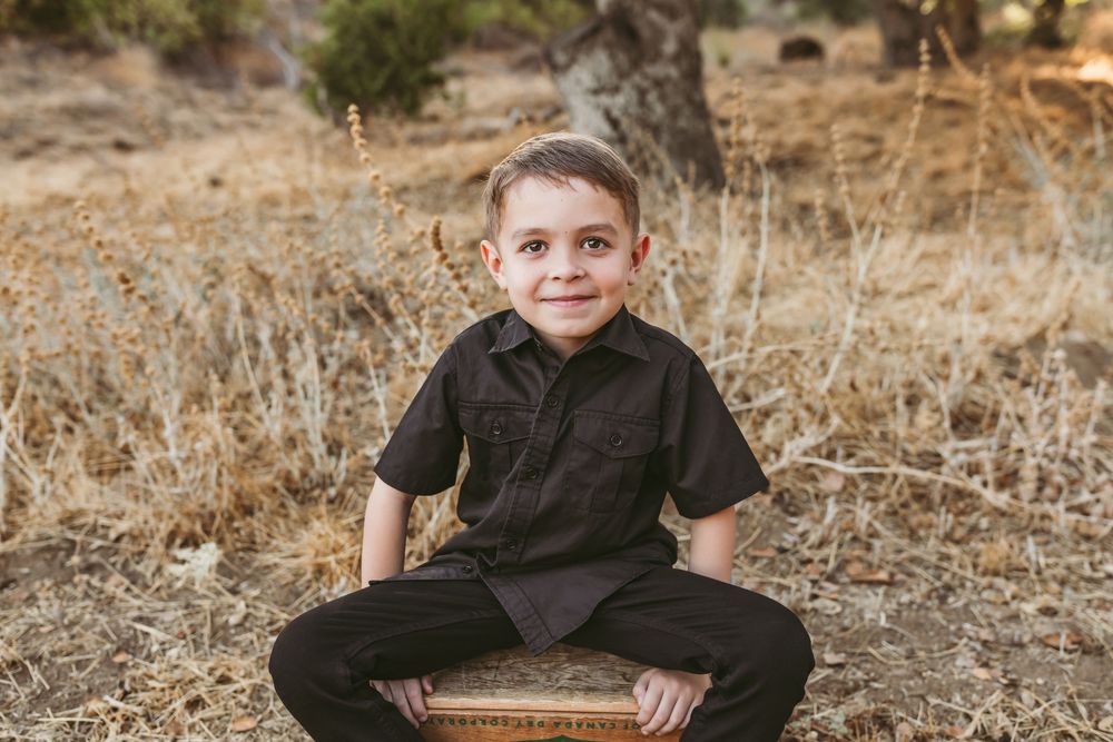 Person wearing dark clothes sits on ground in outdoor setting with dry grass and natural surroundings.