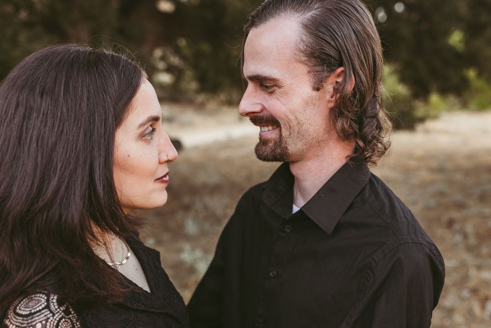 A couple in black attire shares an intimate moment while posing for a portrait outdoors.