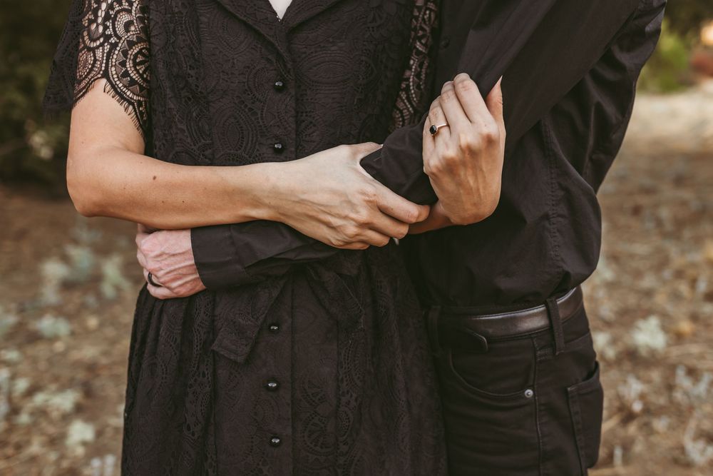 Close-up of hands holding each other against dark clothing in outdoor setting.
