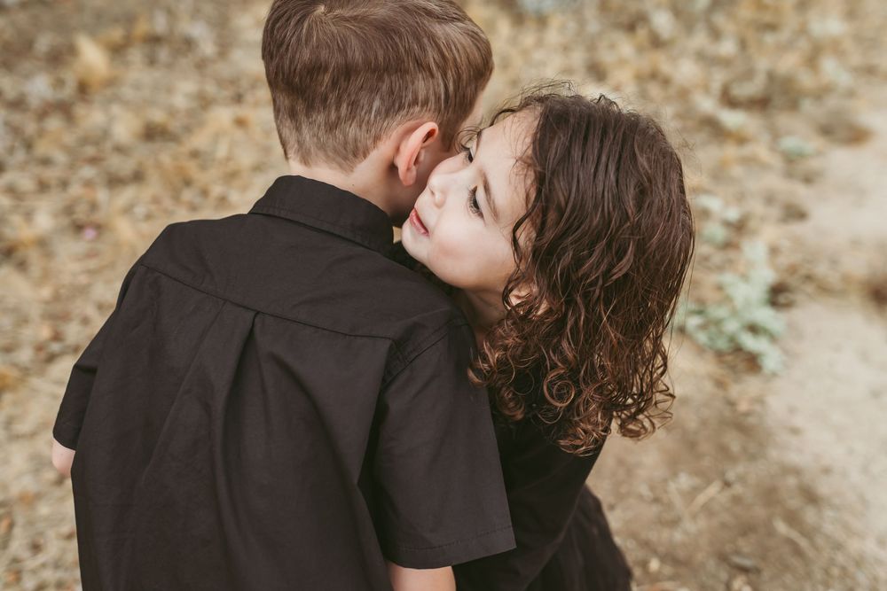 A romantic couple embraces while kissing outdoors in a natural desert setting during golden hour.