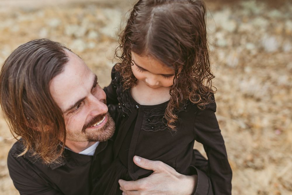 A parent and child share a tender moment outdoors while dressed in black clothing.