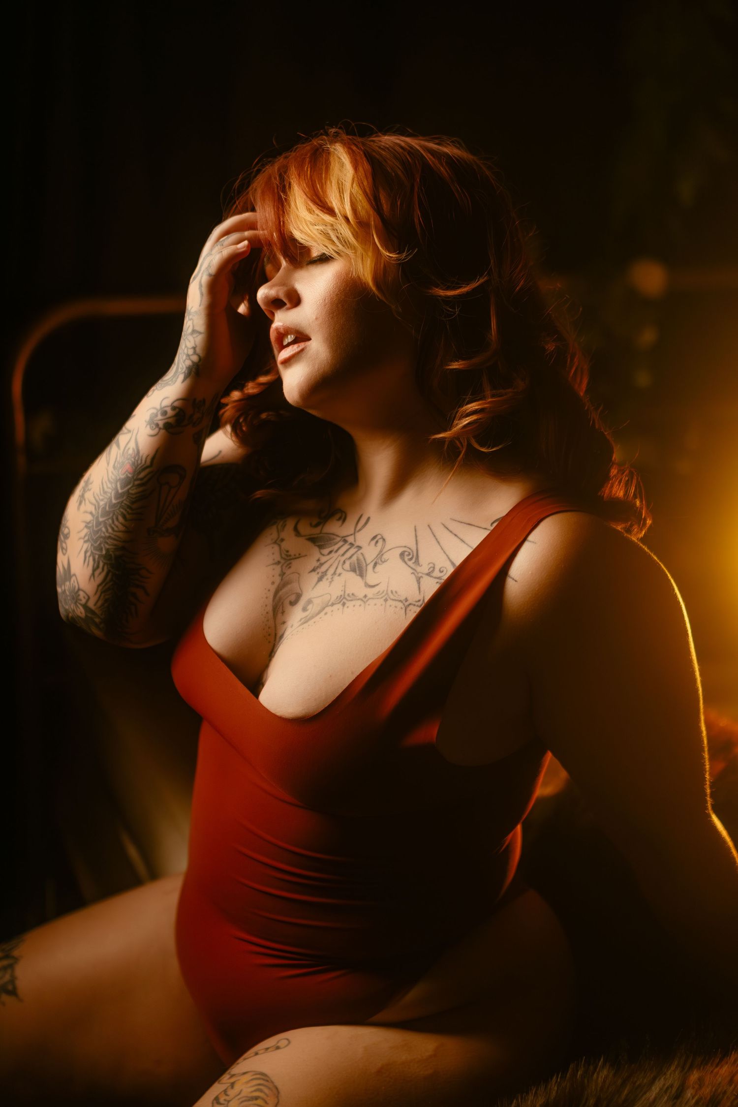 A dramatic moody boudoir photo featuring someone in a red tank top against a dark background with warm lighting at Fort Worth studio.