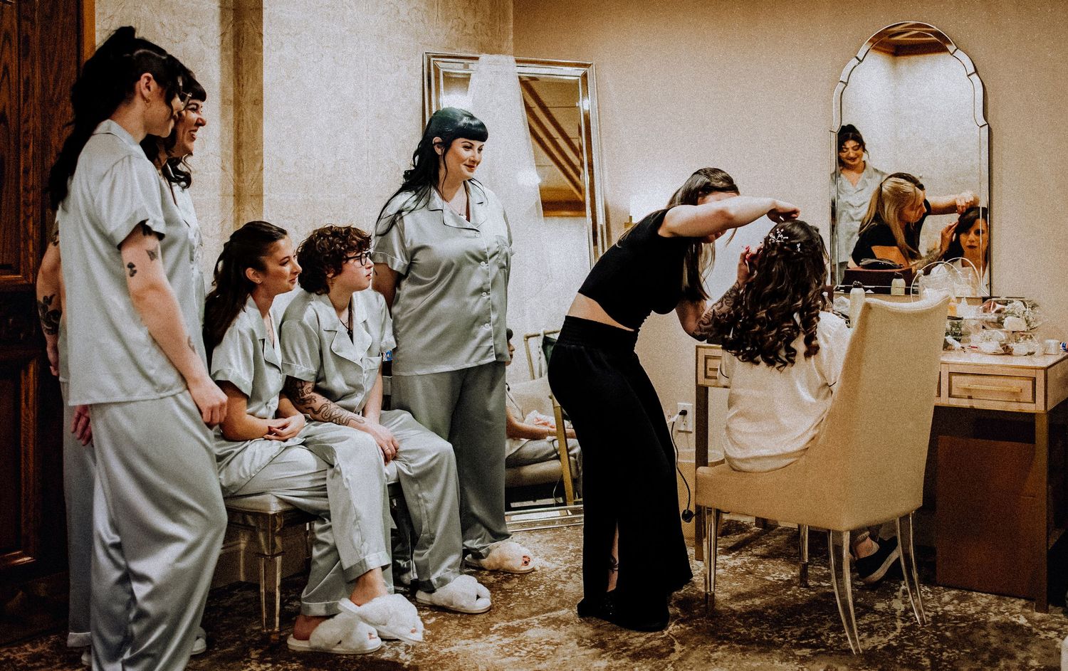 Wedding preparation scene shows people in matching white outfits getting ready in a dressing room with mirrors and chairs.