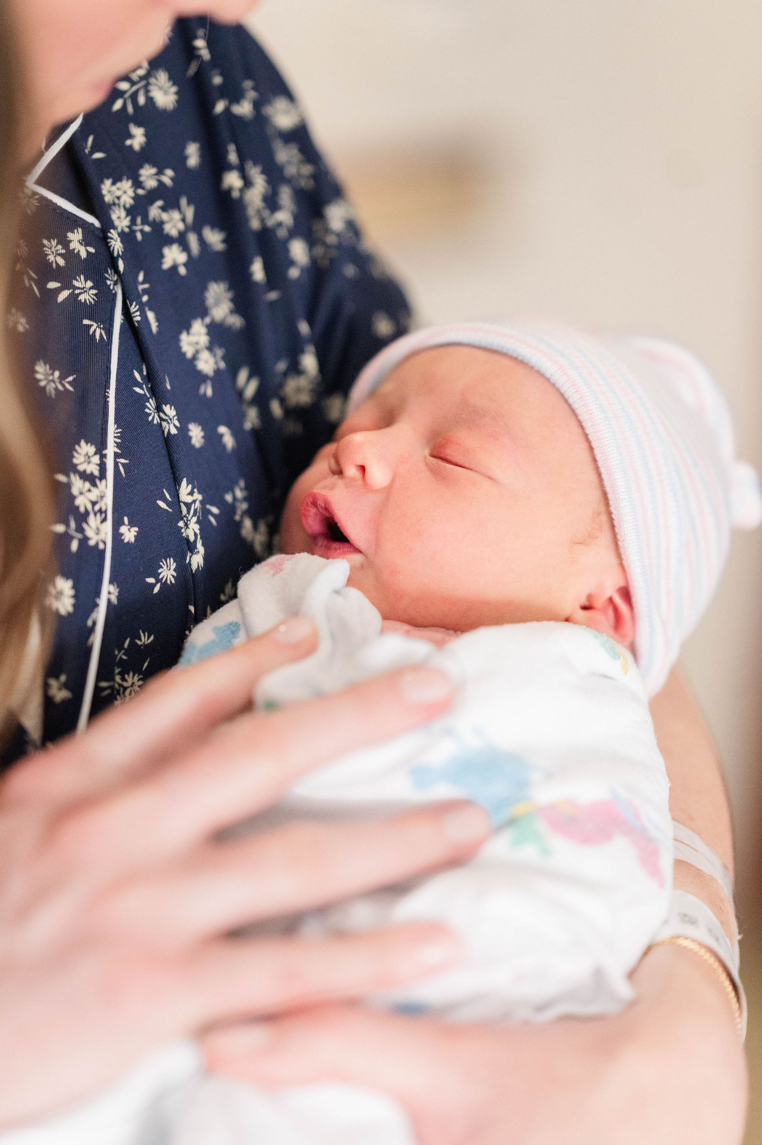 A sleeping newborn baby wearing a white hat lies peacefully against floral patterned fabric.