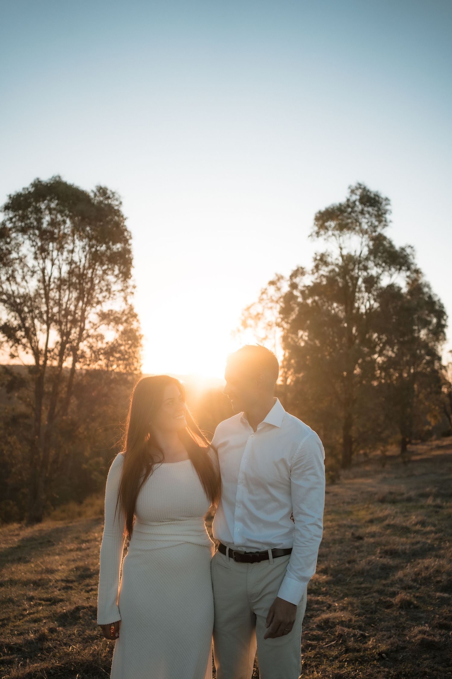 Silhouetted couple embraces at sunset with eucalyptus trees in background during golden hour photography session.