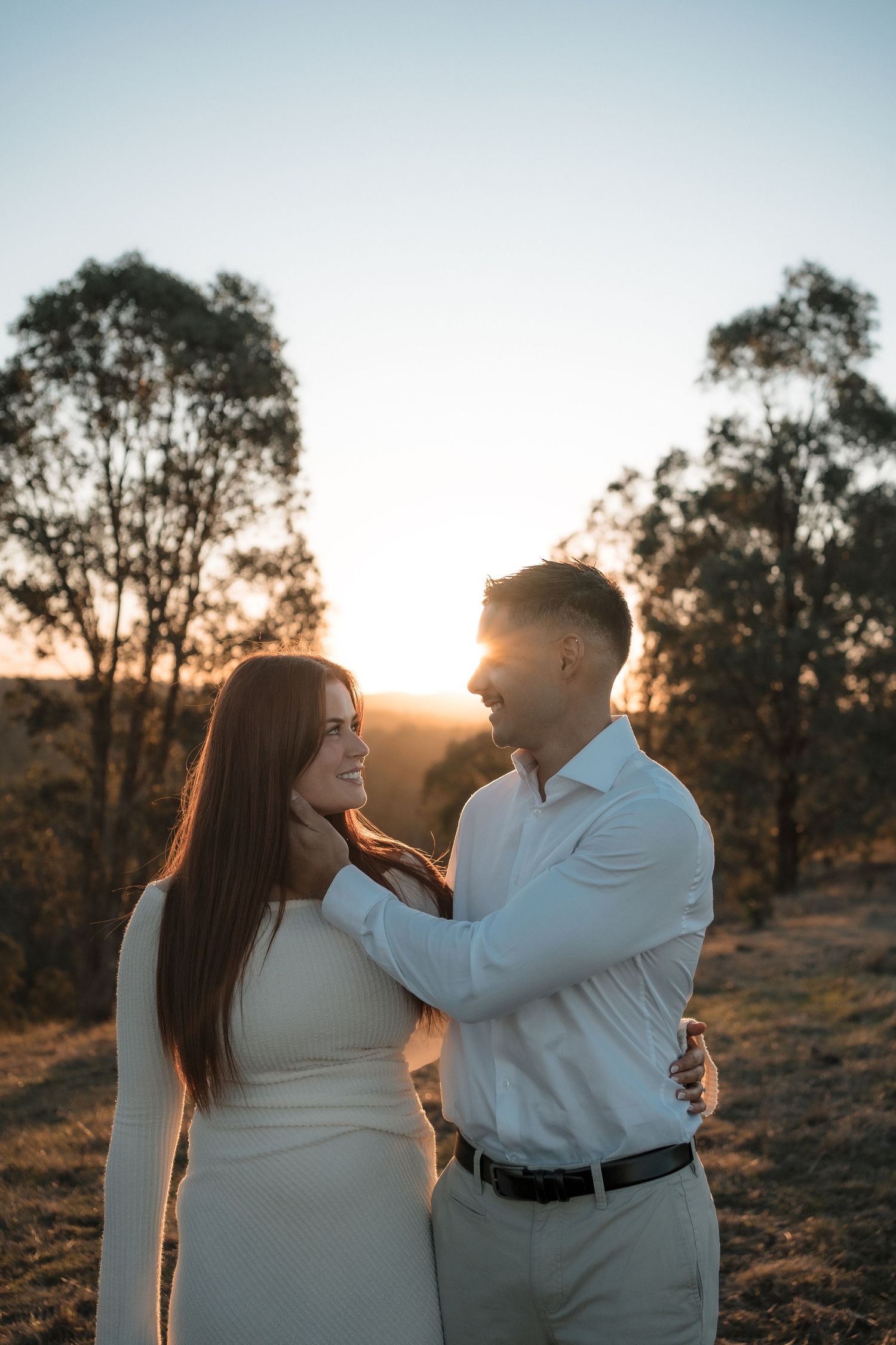 A couple shares an intimate moment at sunset with eucalyptus trees in the background.