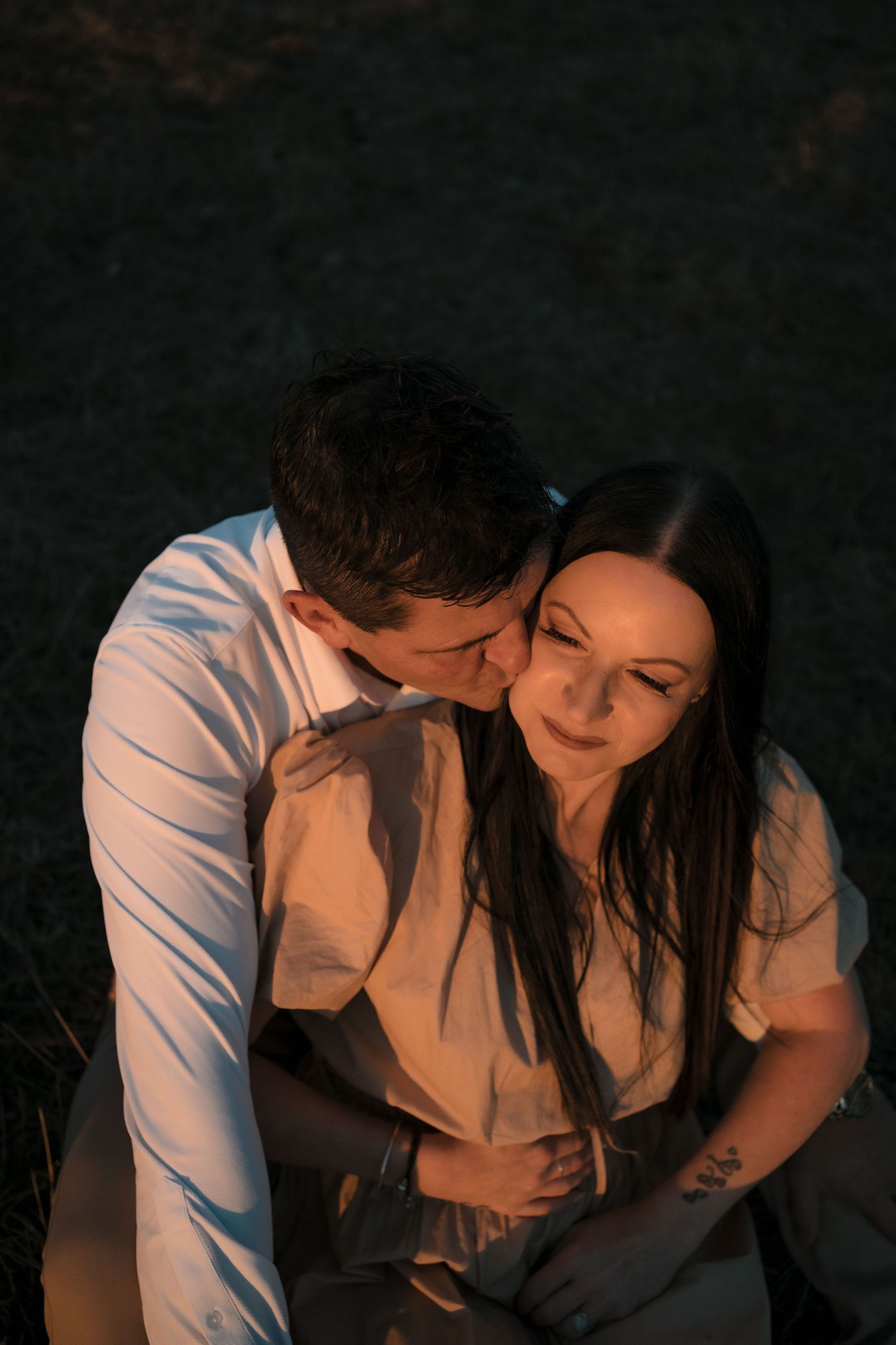 A romantic couple sharing an intimate moment in warm lighting against a dark background.