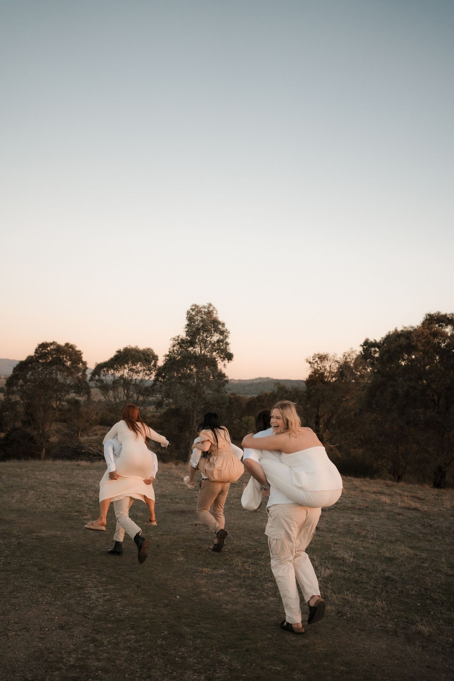 Three figures in white garments joyfully jumping on a hilltop at sunset.