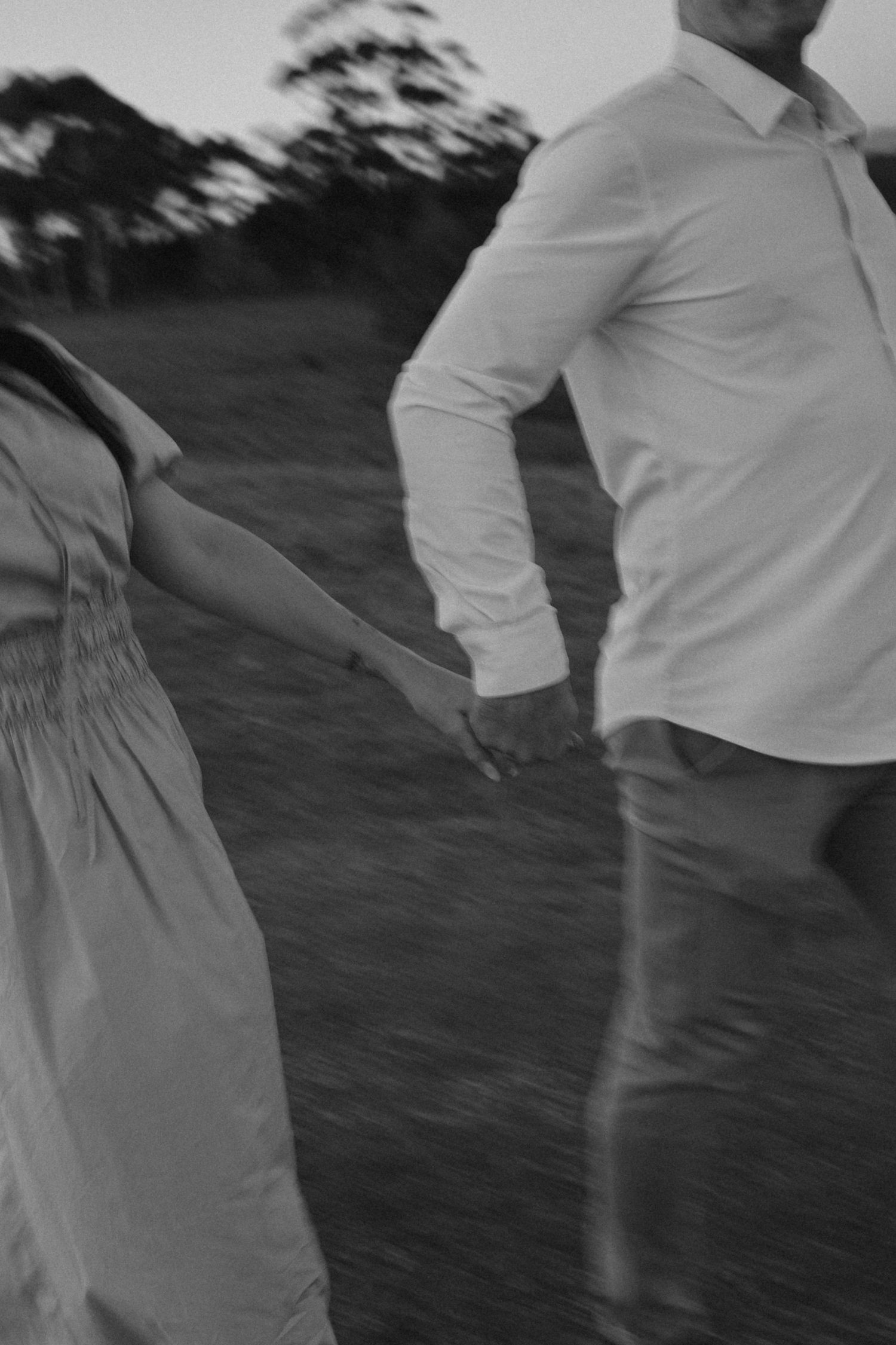 Motion-blurred black and white photo of two people in light colored clothing dancing outdoors at dusk.