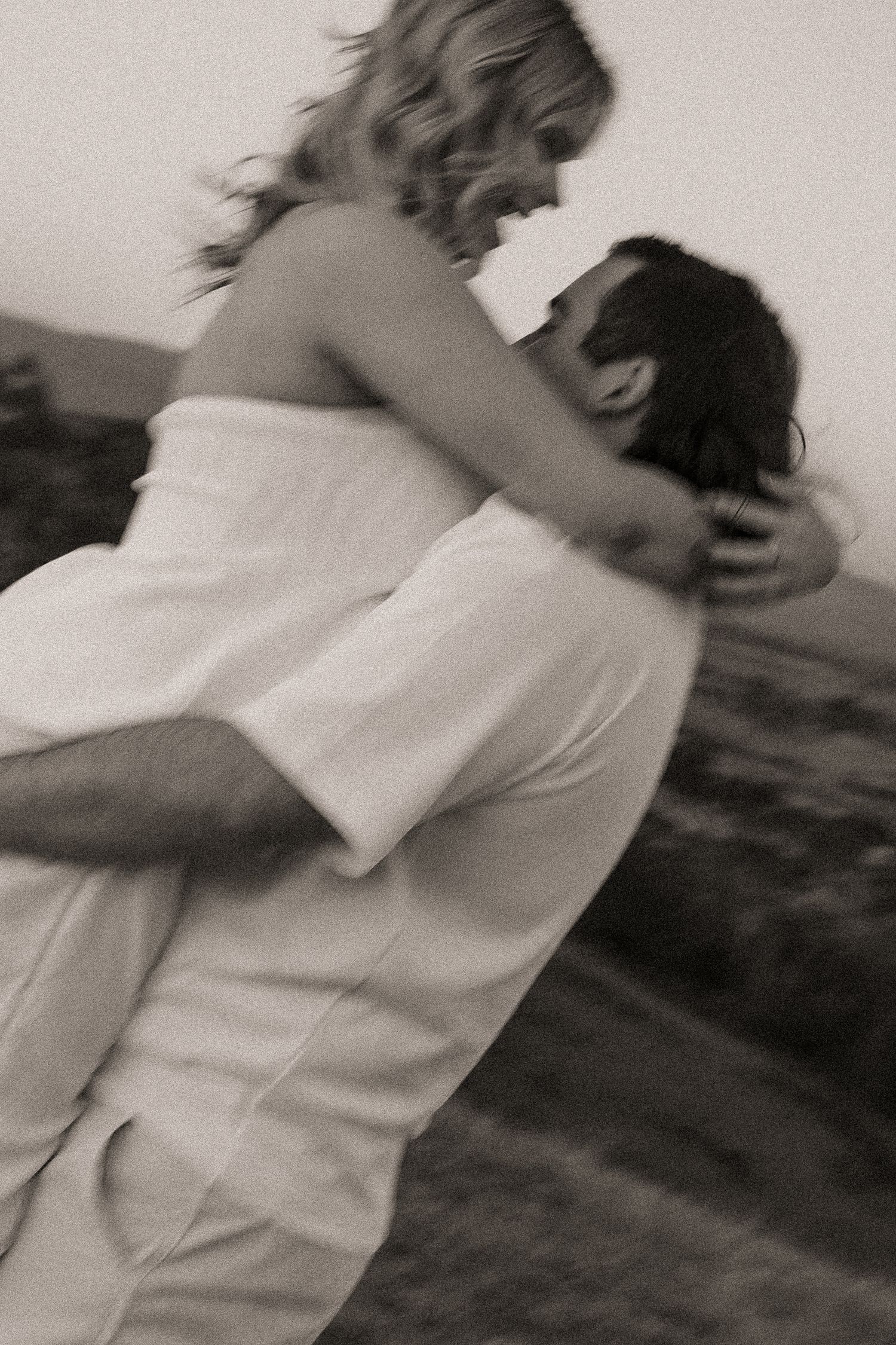 A romantic black and white photo shows a couple embracing in an intimate moment outdoors.
