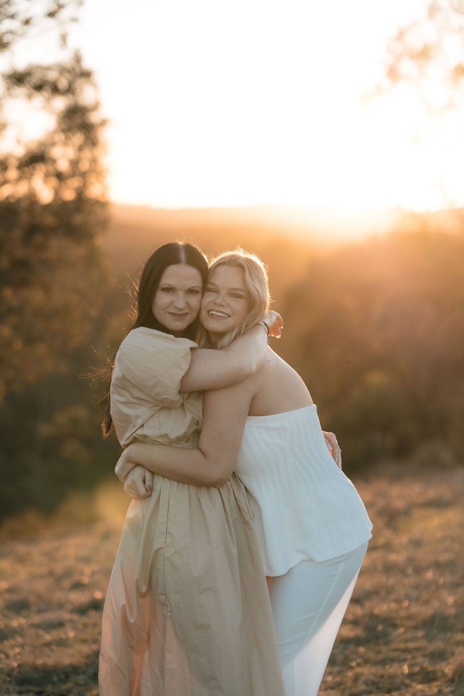 Two people hugging and laughing together in a sun-drenched field at sunset.