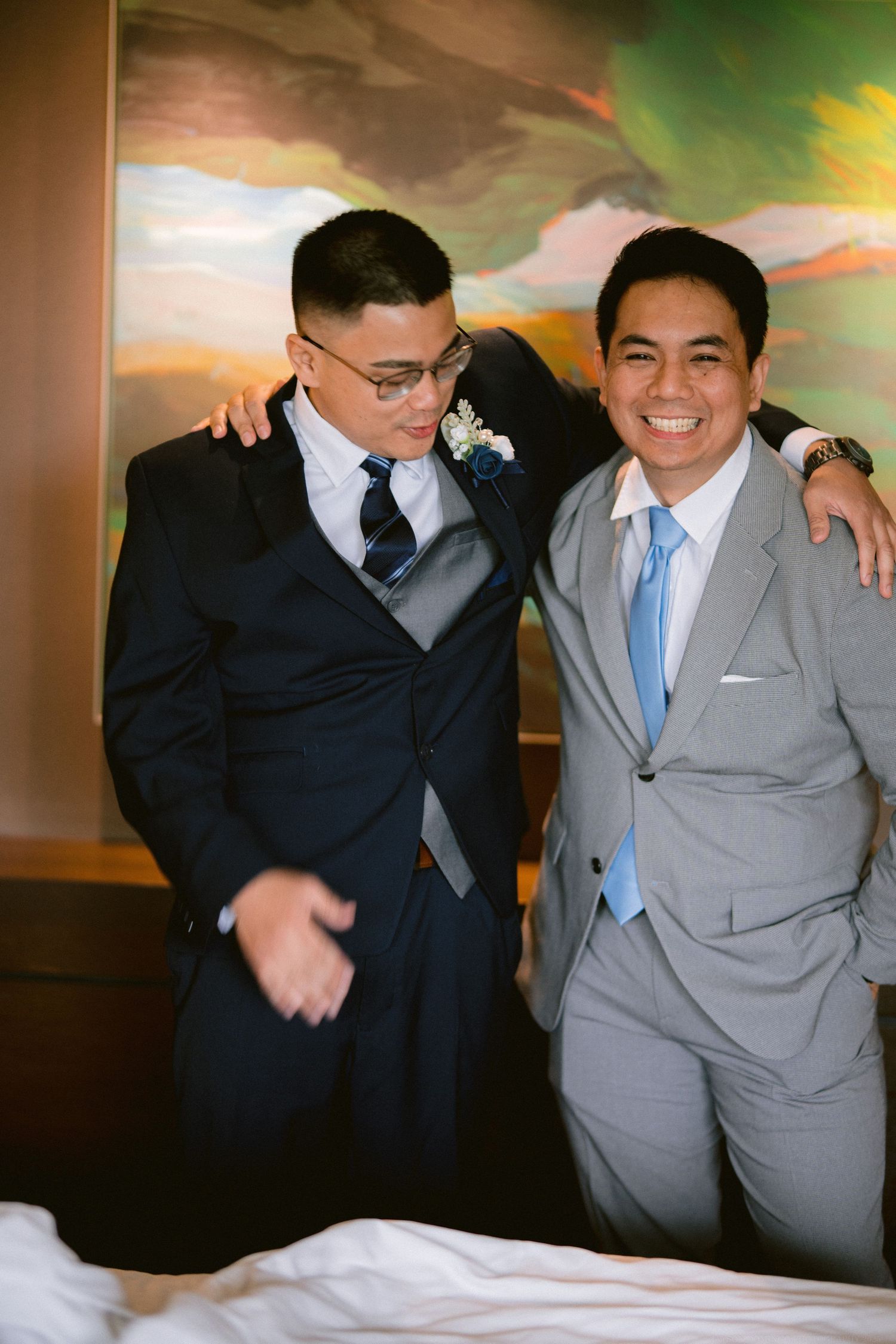 Two young men in formal suits share a joyful moment together against a colorful backdrop.