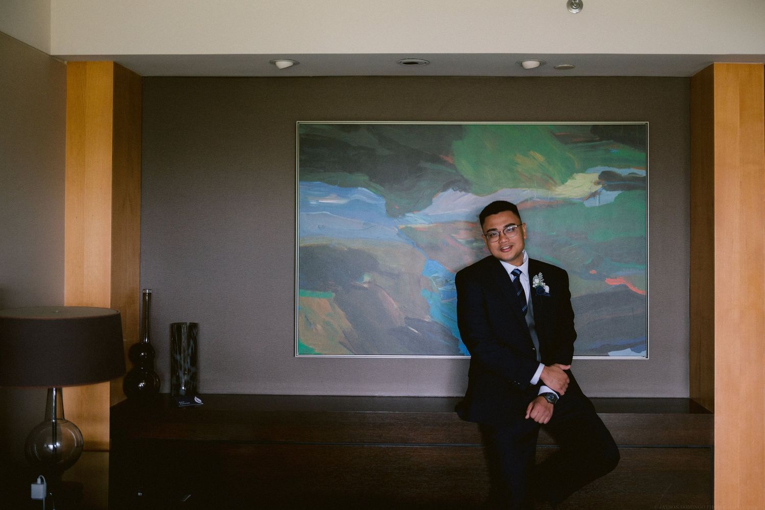 A person in a formal suit sits in front of a colorful wall mural.