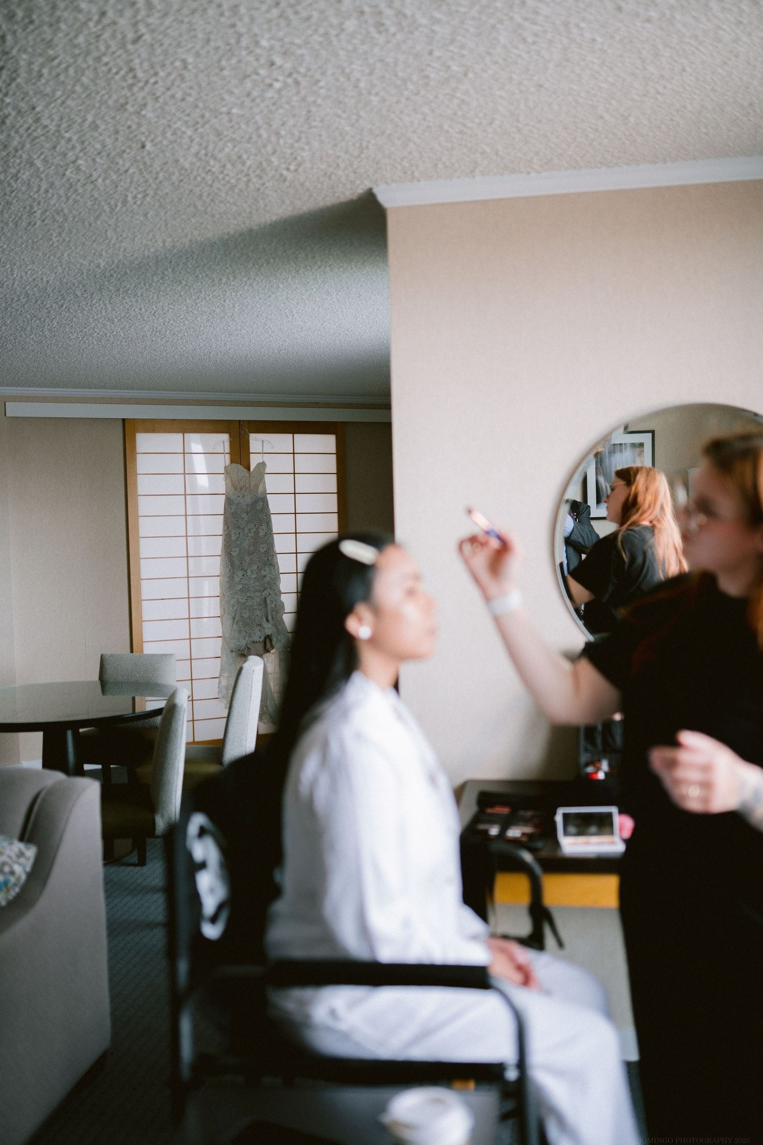 Wedding preparation scene showing a makeup artist styling in front of a shoji screen backdrop.